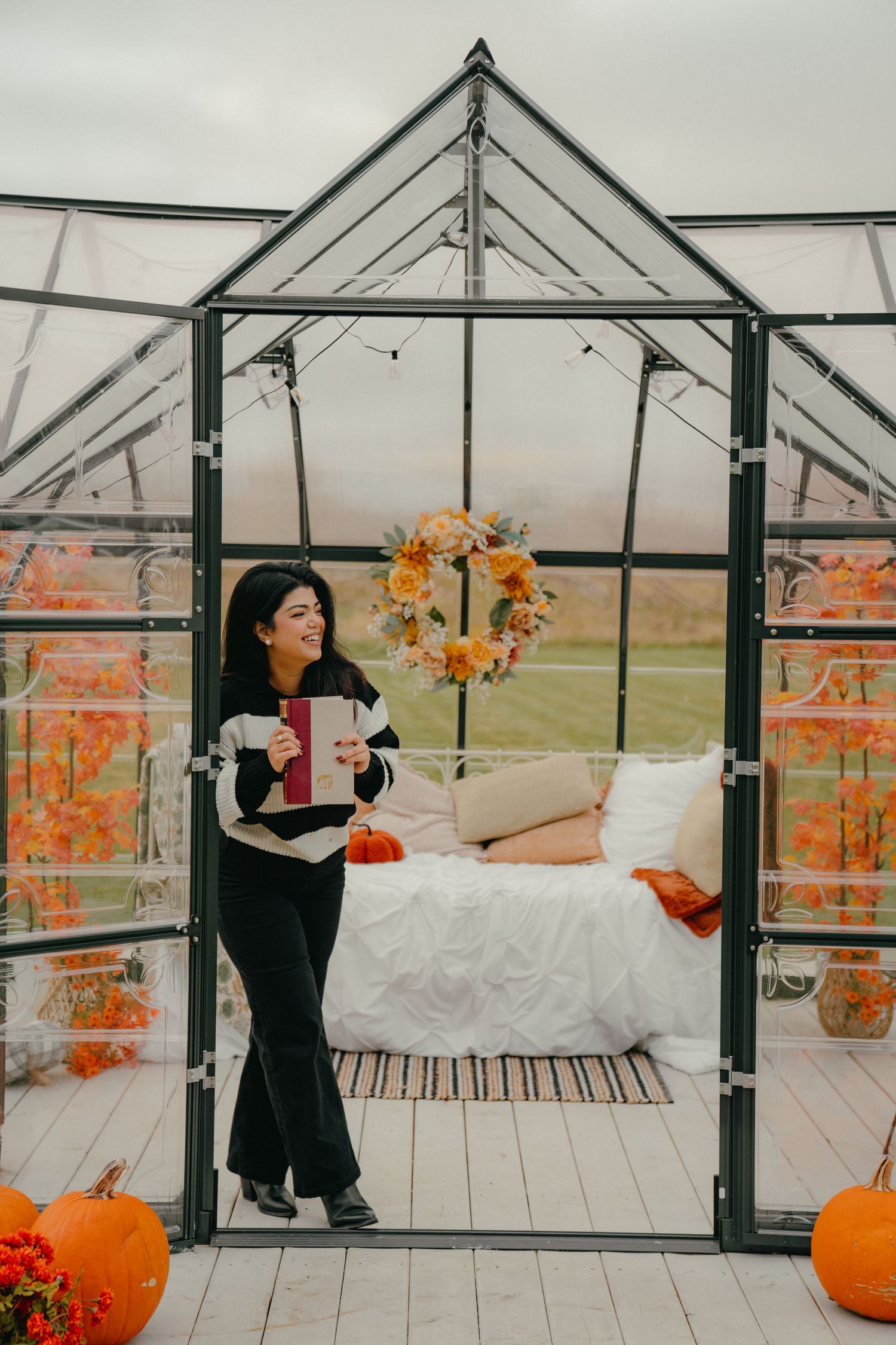 Greenhouse setting with pumpkins and fall decor featuring someone in black clothing.