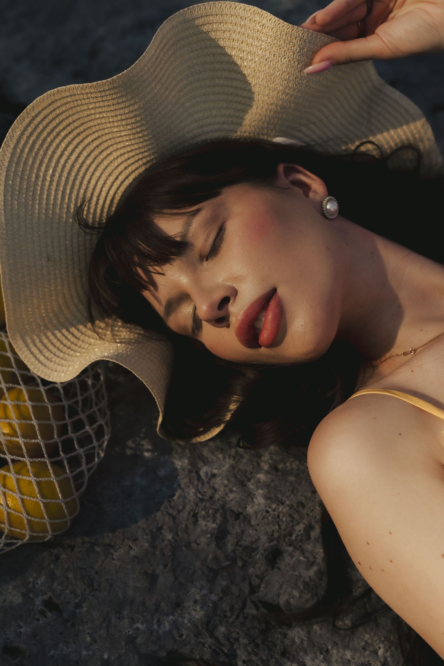 Artistic portrait with a wide-brimmed straw hat creating dramatic shadows in moody lighting.
