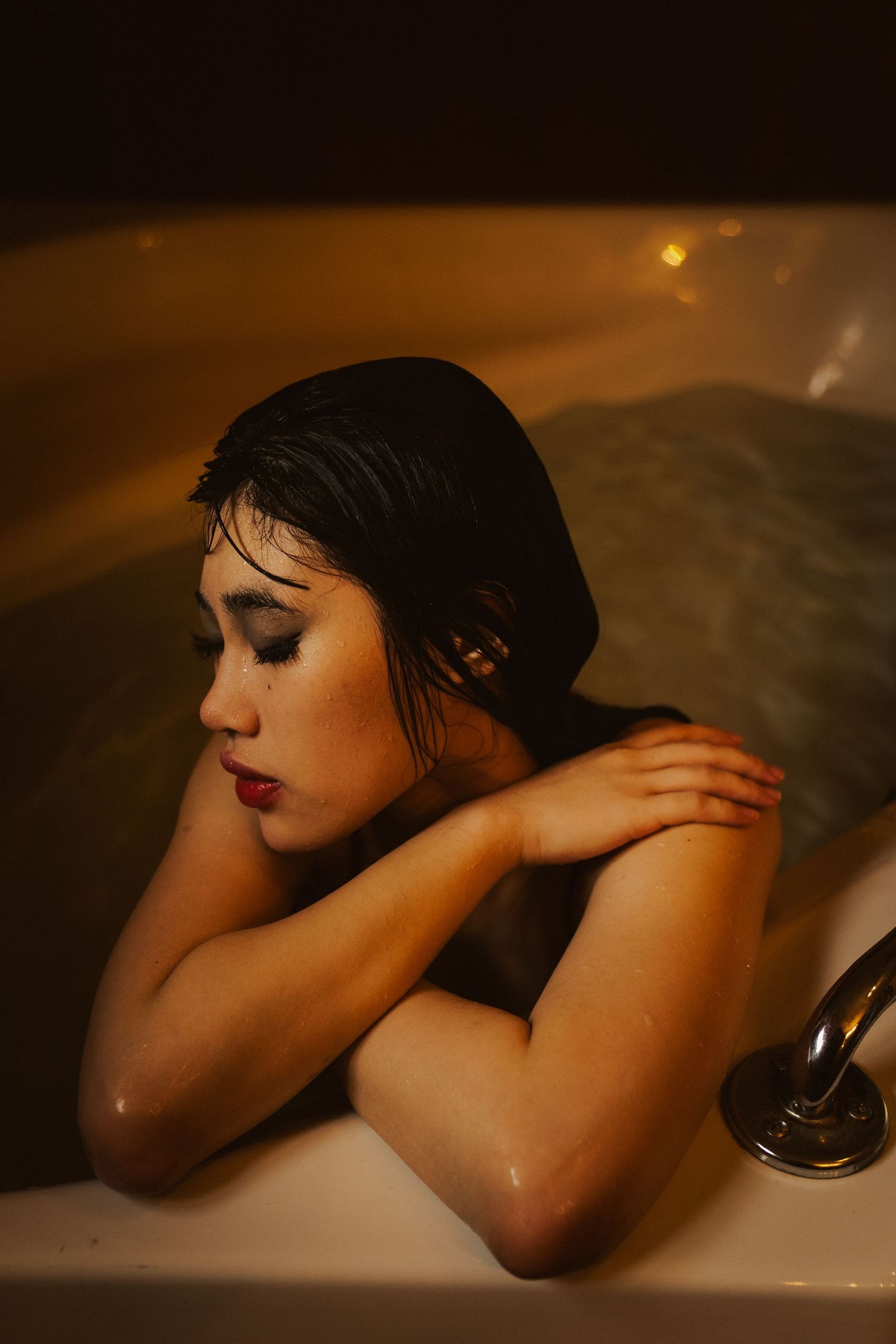 Artistic bathtub portrait with moody lighting and water reflections.