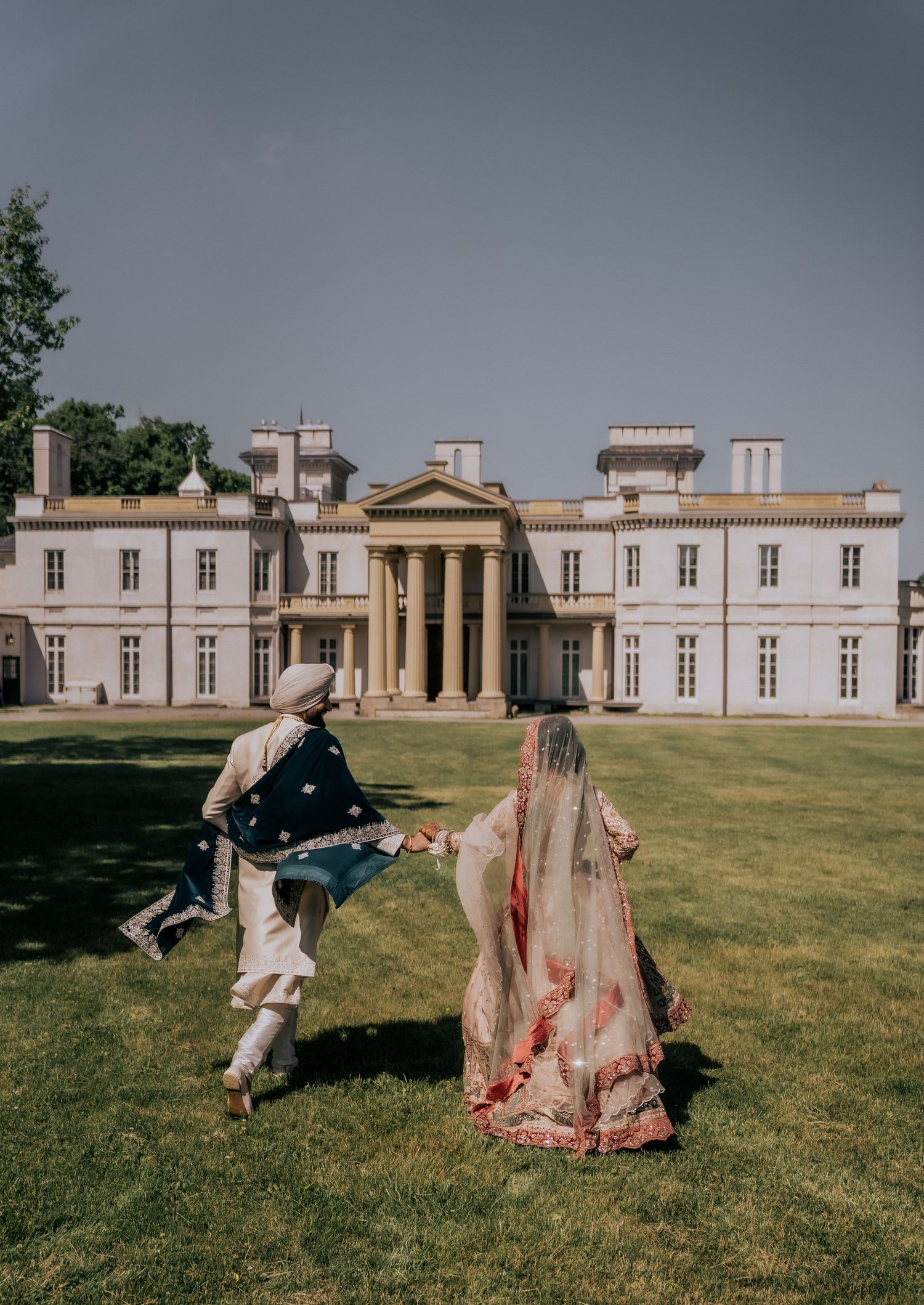 Couple in traditional period costumes dancing on lawn in front of neoclassical mansion with dramatic stormy sky.