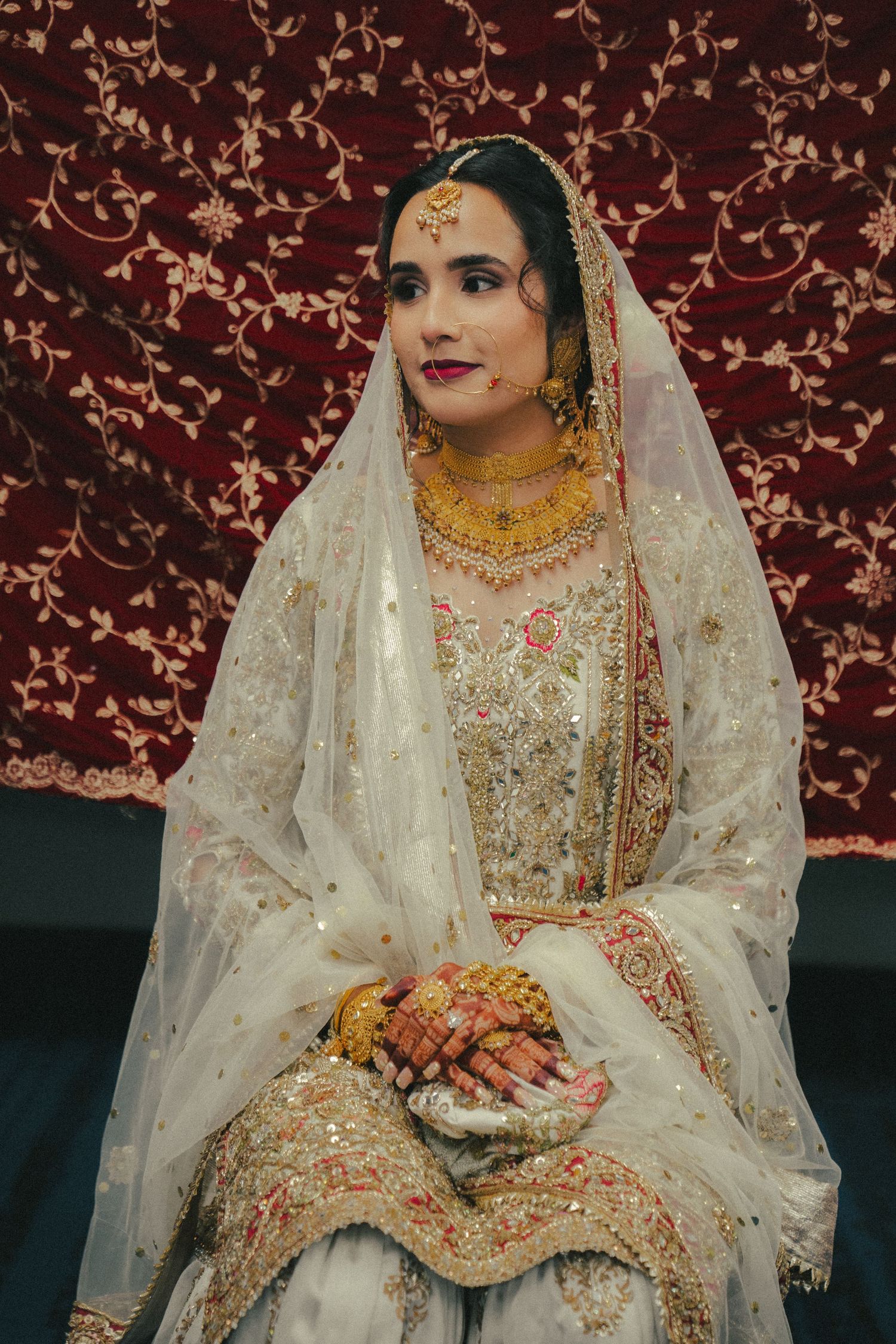Traditional South Asian bride wearing elaborate gold jewelry and cream embroidered outfit.