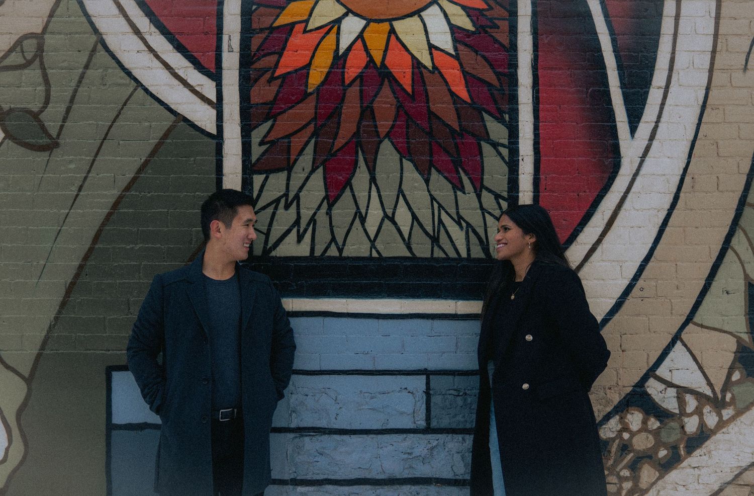 People posing against a colorful wall with geometric sun pattern artwork.