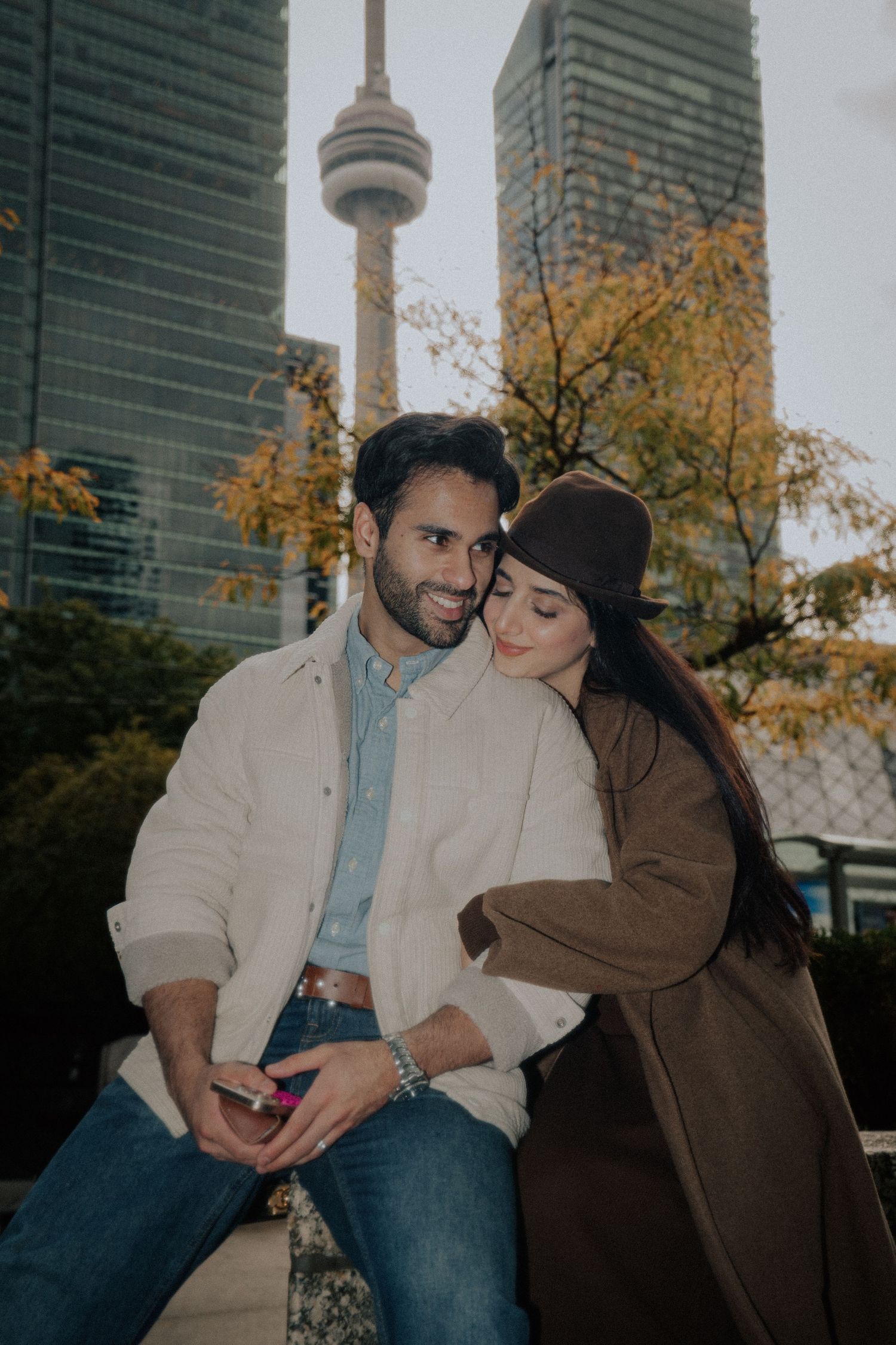 A romantic autumn scene with a couple embracing near tall buildings and fall foliage.