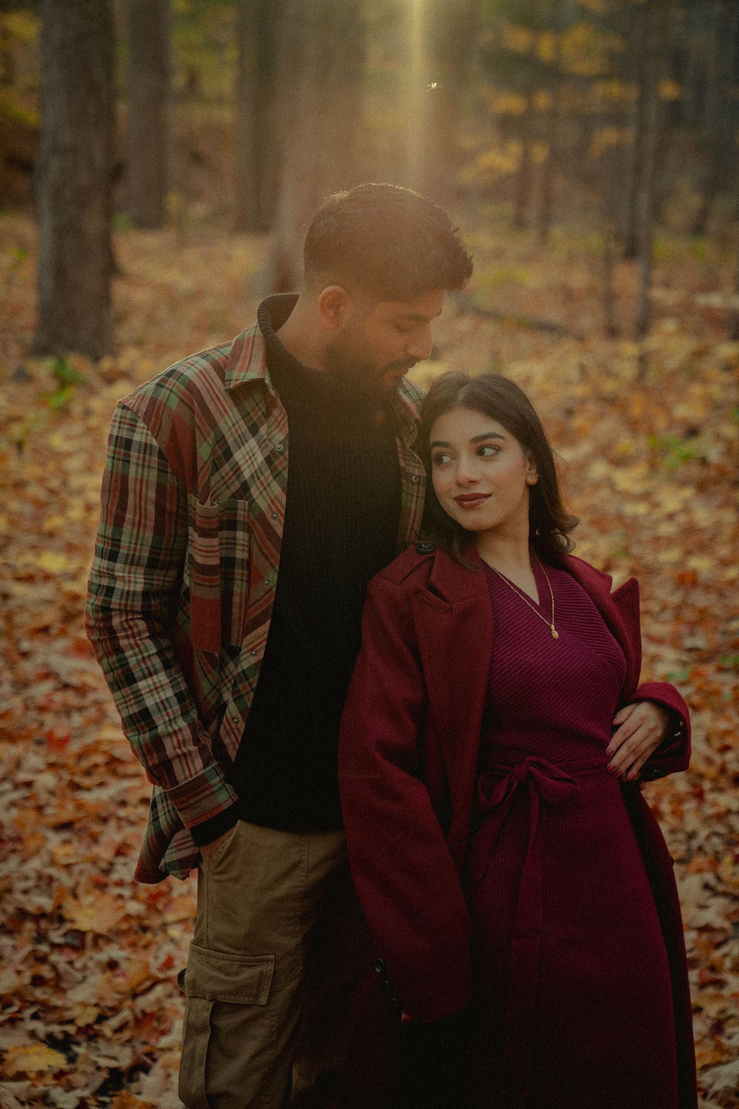 Romantic autumn couple photoshoot with burgundy and plaid outfits among fallen leaves.