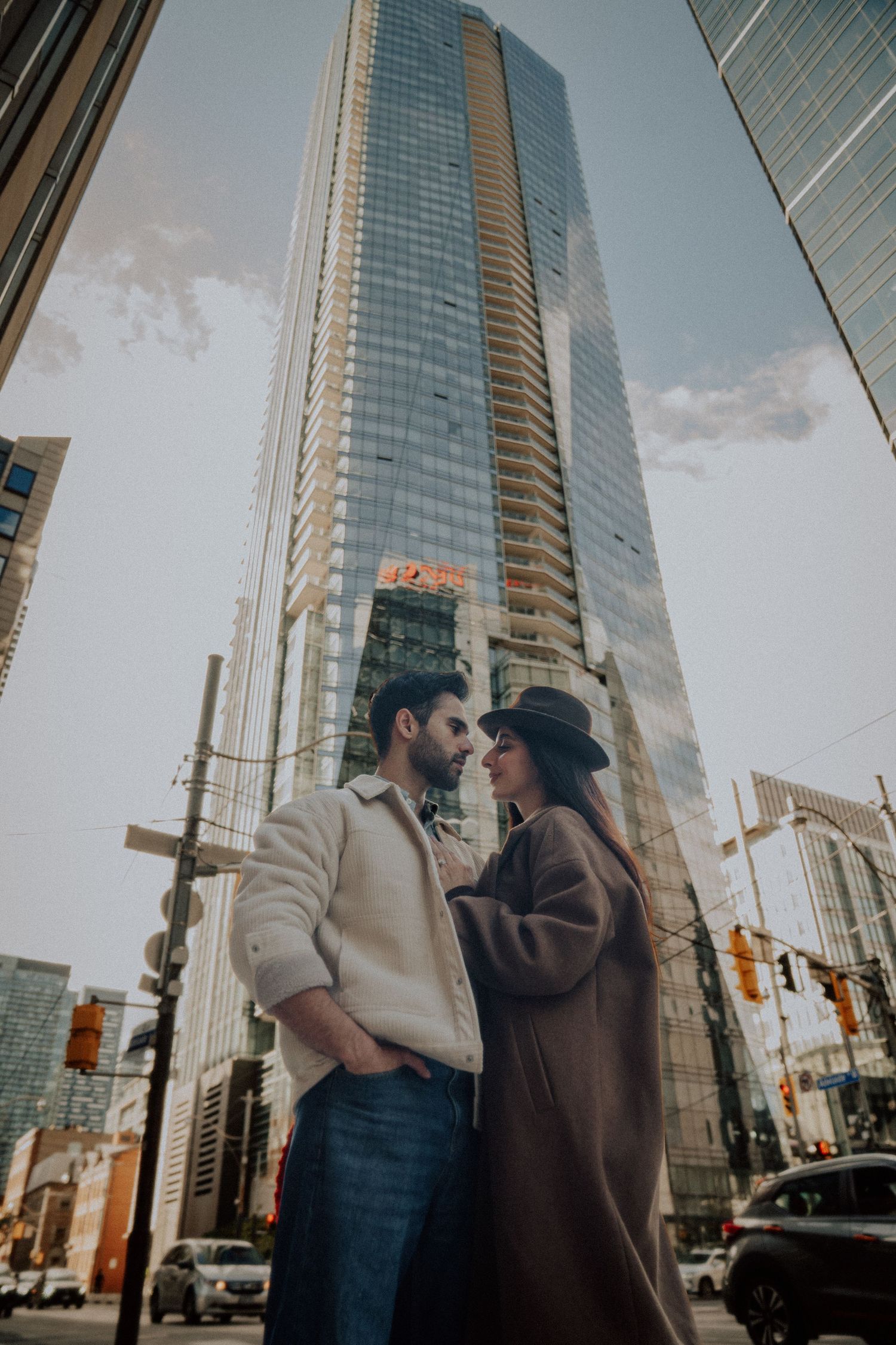 A couple shares an intimate moment against the backdrop of modern glass skyscrapers in an urban setting.