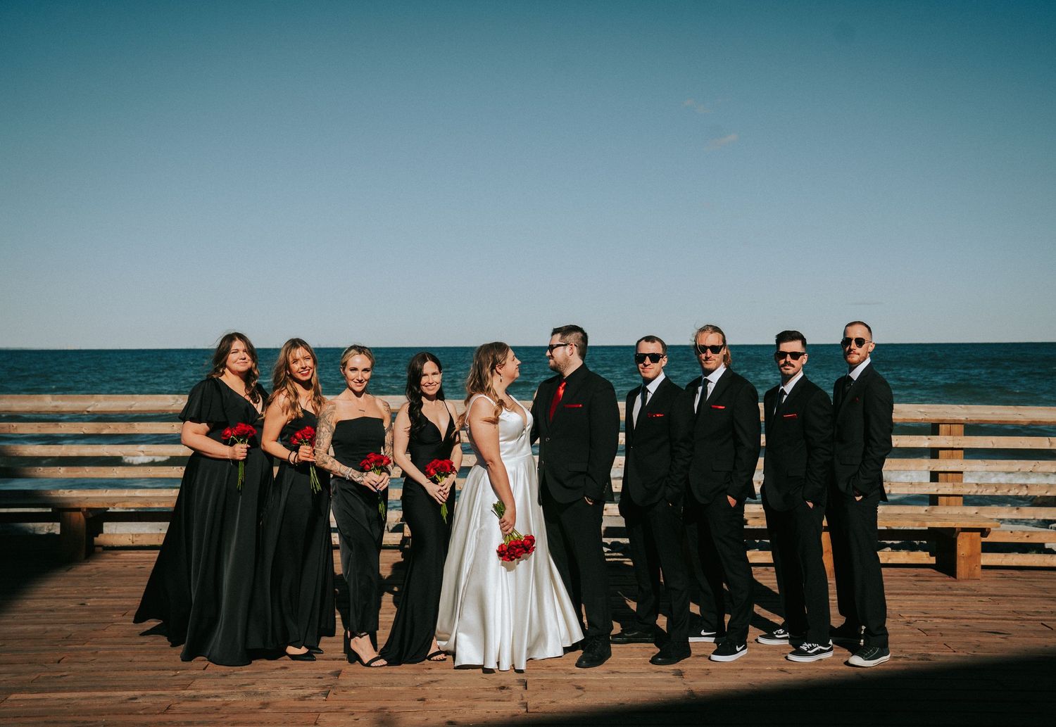 Wedding party lined up on boardwalk against ocean backdrop.