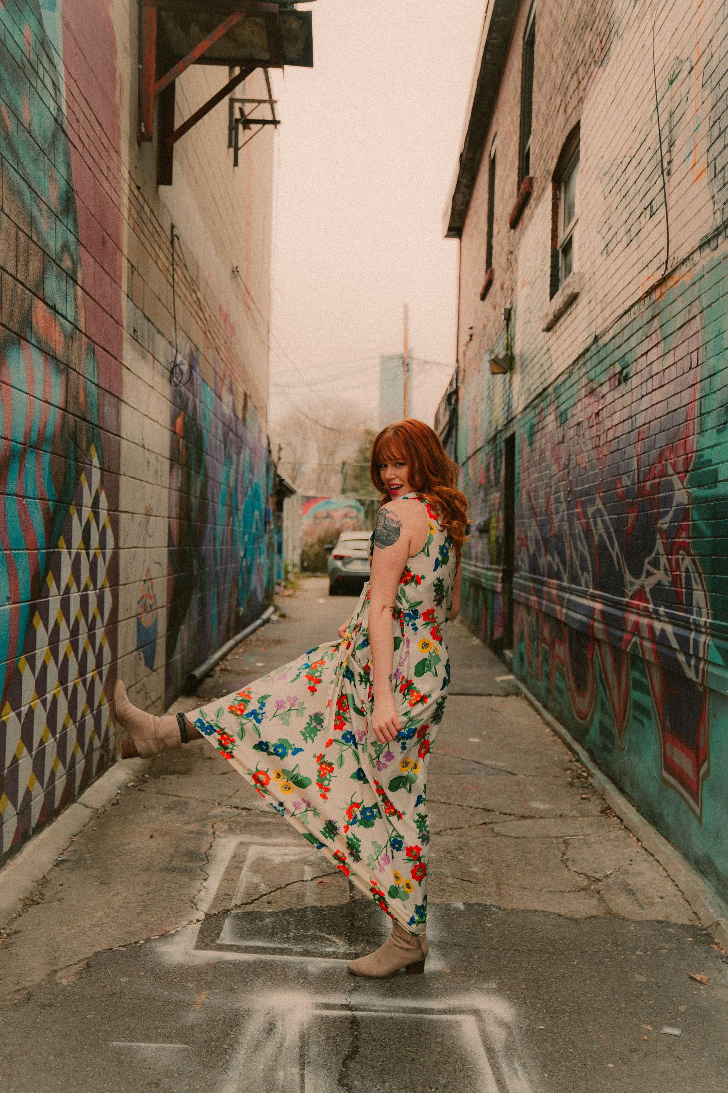Retro-styled fashion shoot in floral dress against urban alley backdrop.