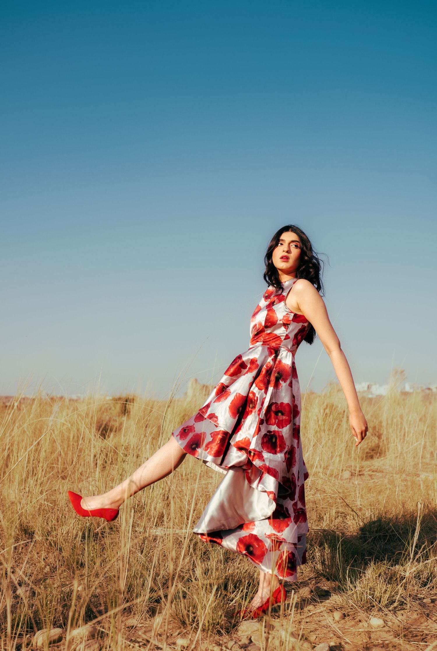 Dynamic poses in floral dress amidst golden field.