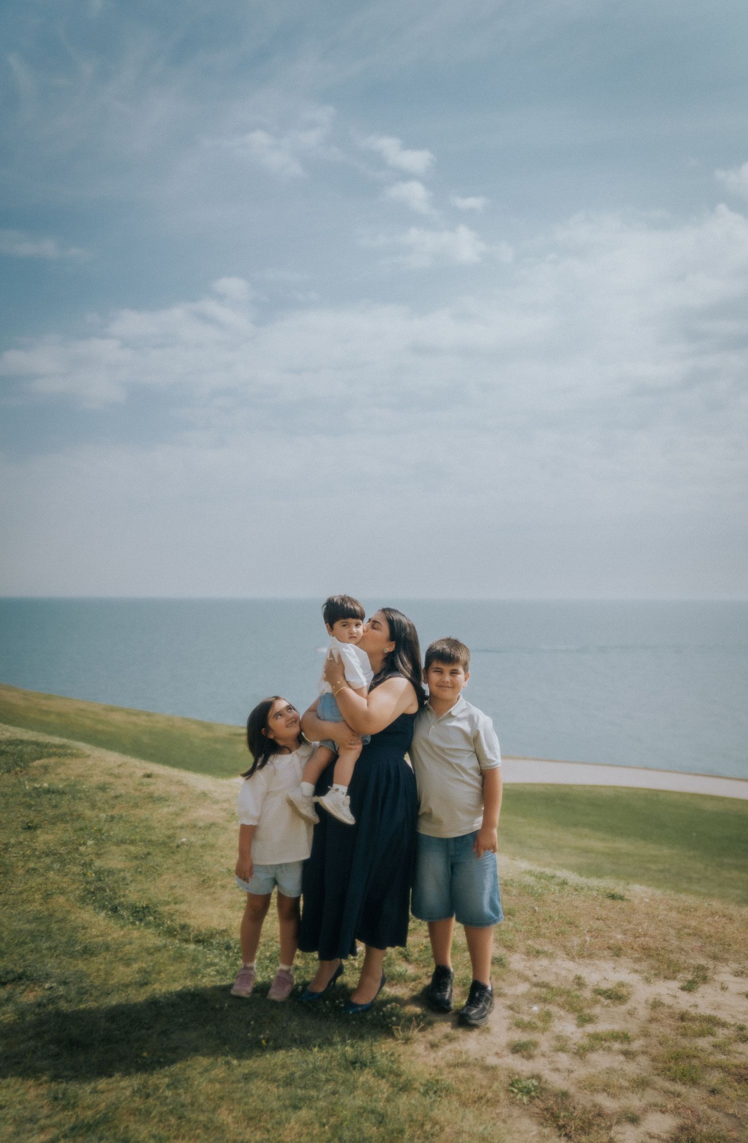 A group poses together on a coastal hillside overlooking the ocean on a cloudy day.