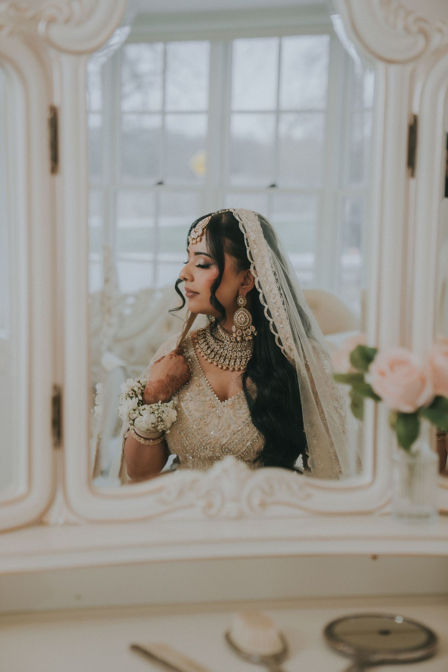 Traditional South Asian bridal attire with ornate jewelry and veil in an elegant indoor setting.