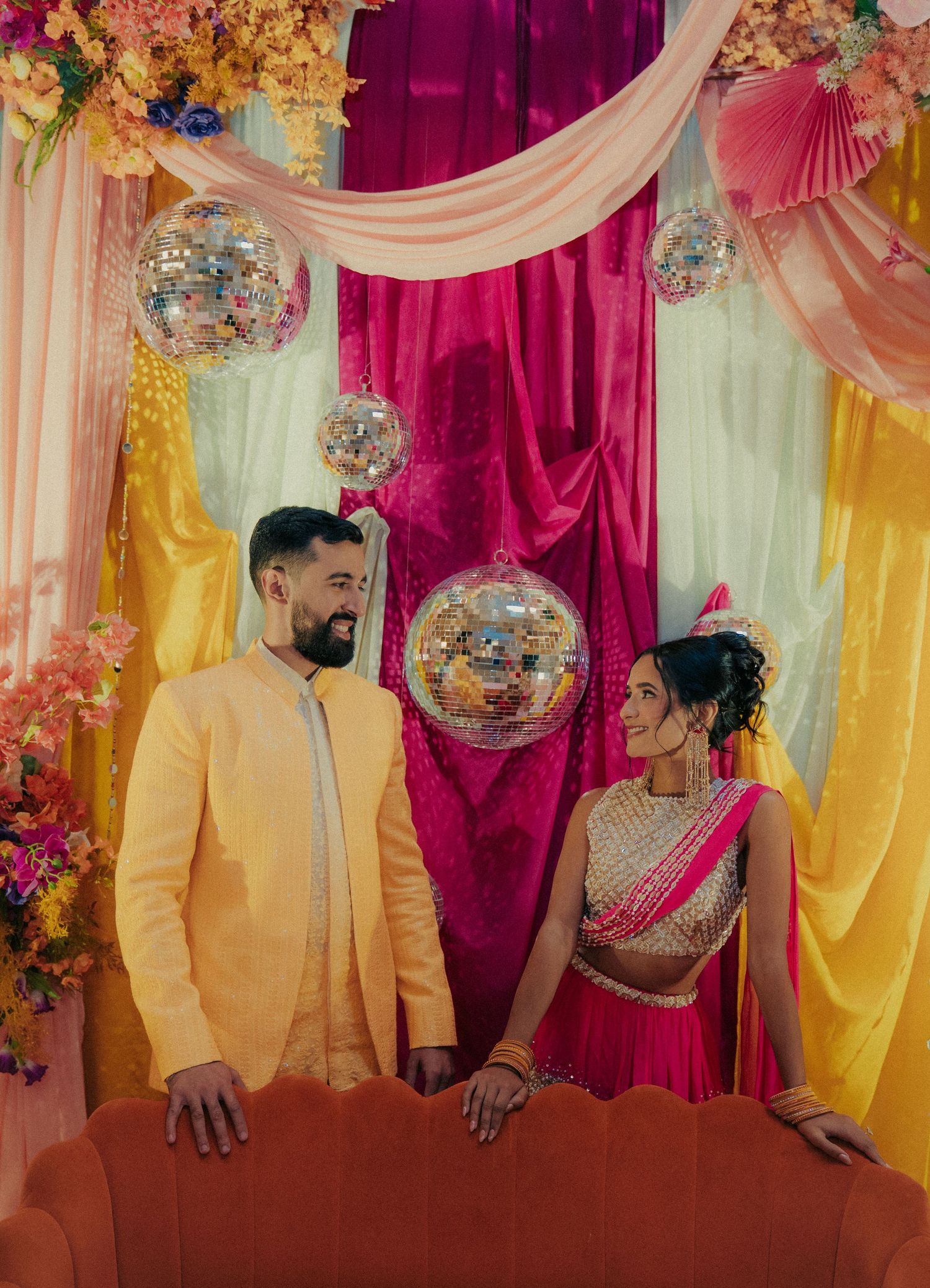 A couple poses against a colorful backdrop with pink, yellow and burgundy drapes at a formal event.
