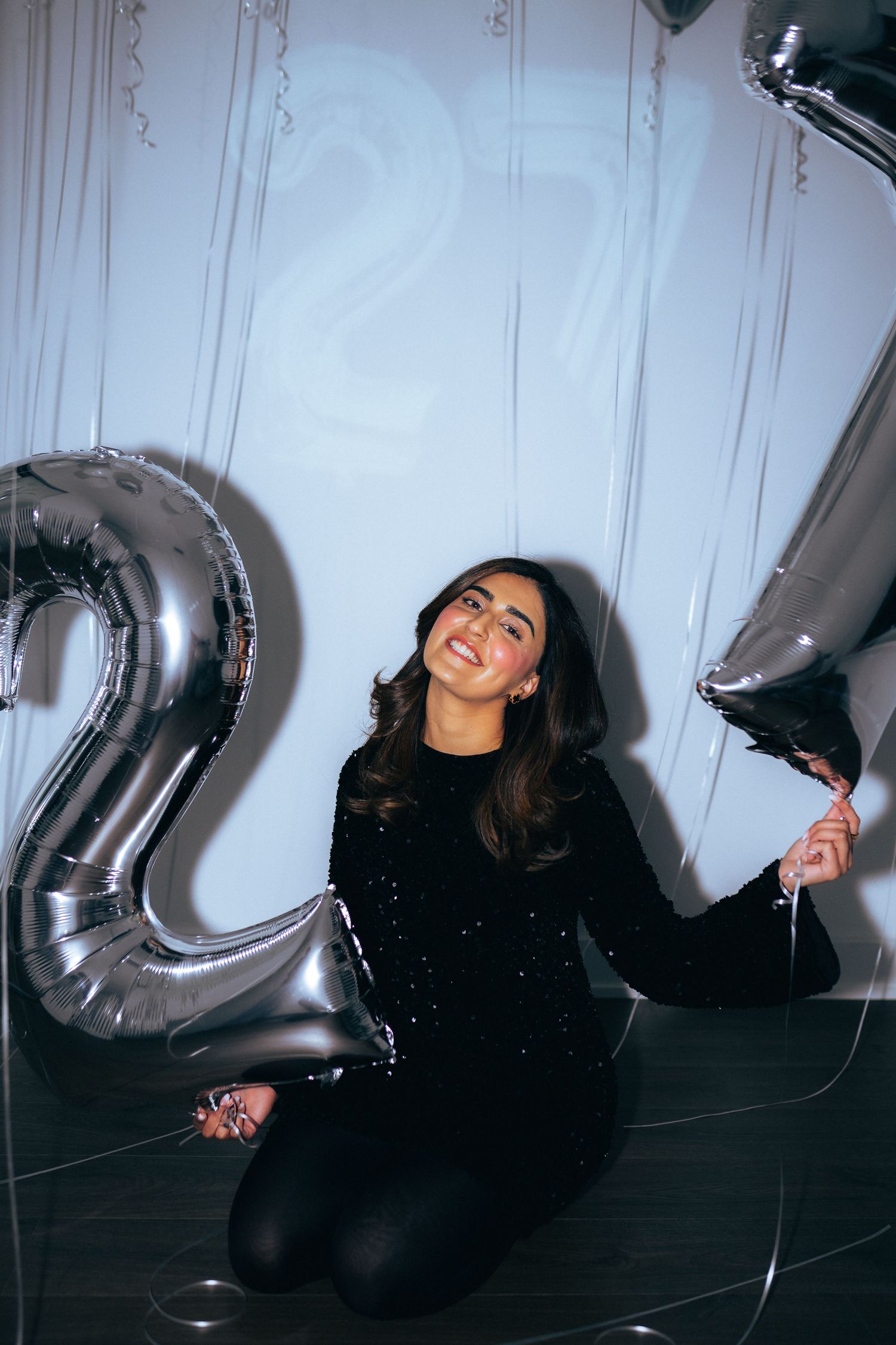 Celebratory scene with silver number balloons against a white wall.
