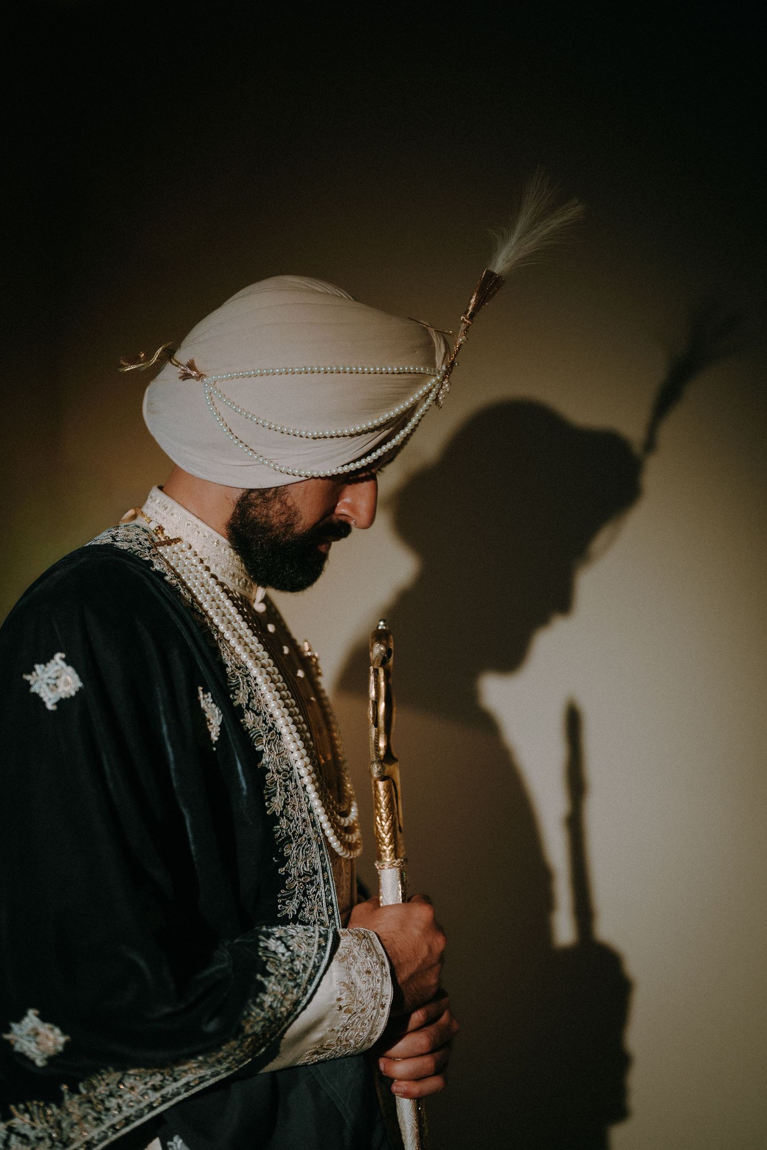 A traditional Sikh groom wearing a white turban and embroidered sherwani in dramatic lighting.