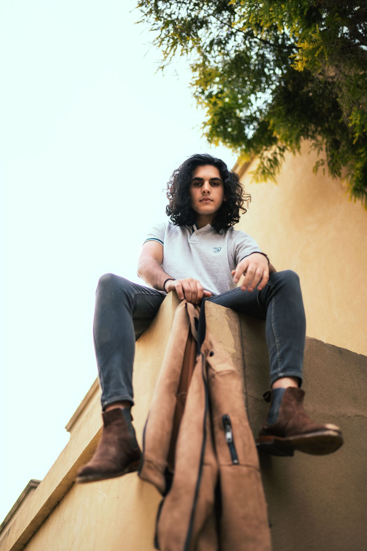 Low-angle portrait series against sky with casual denim and leather styling.