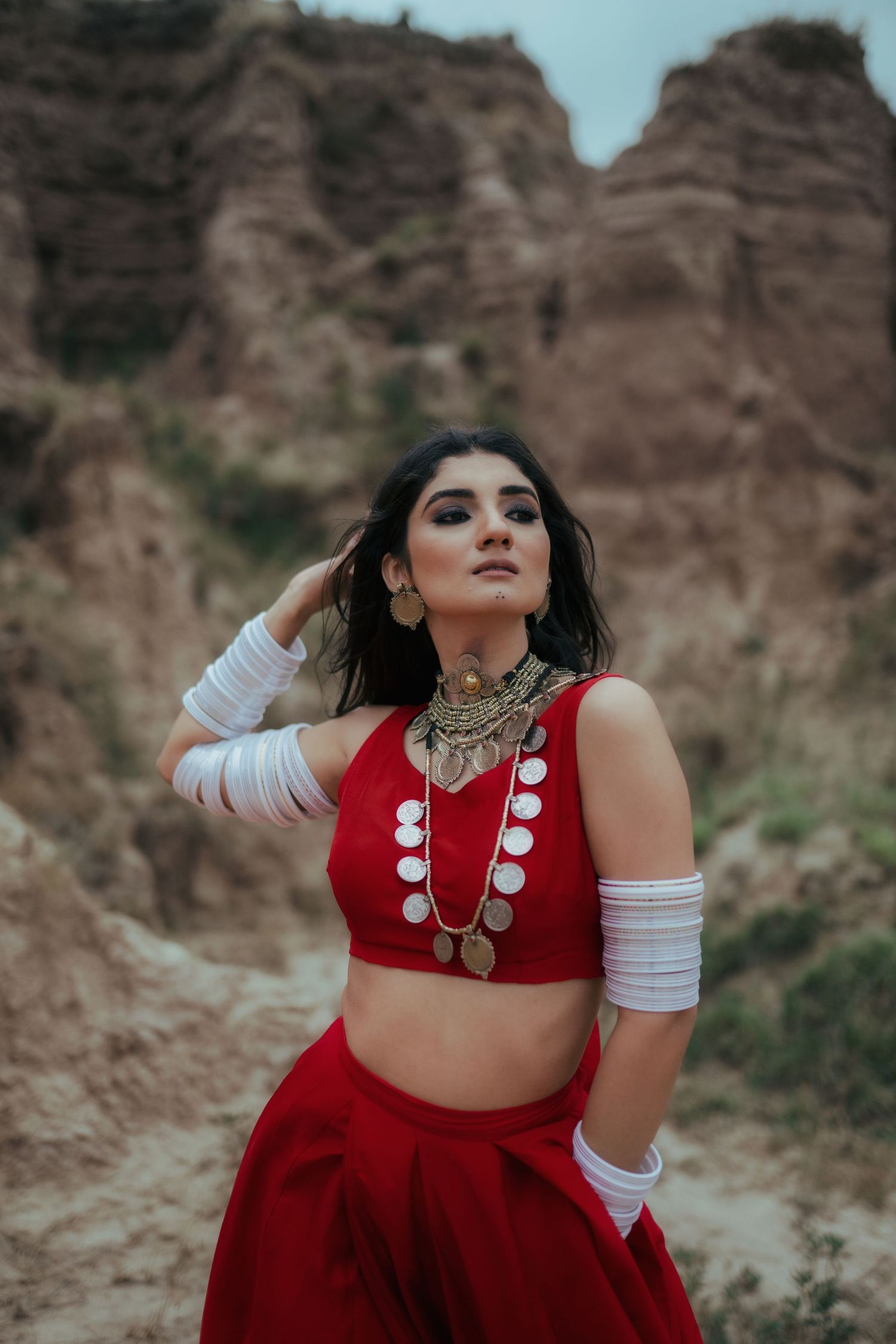 Traditional red outfit with silver jewelry and white arm wraps against desert cliffs.