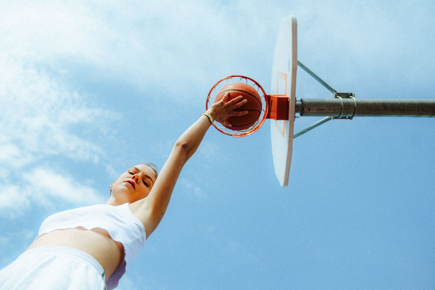 Action shots of basketball player reaching for hoop against blue sky.