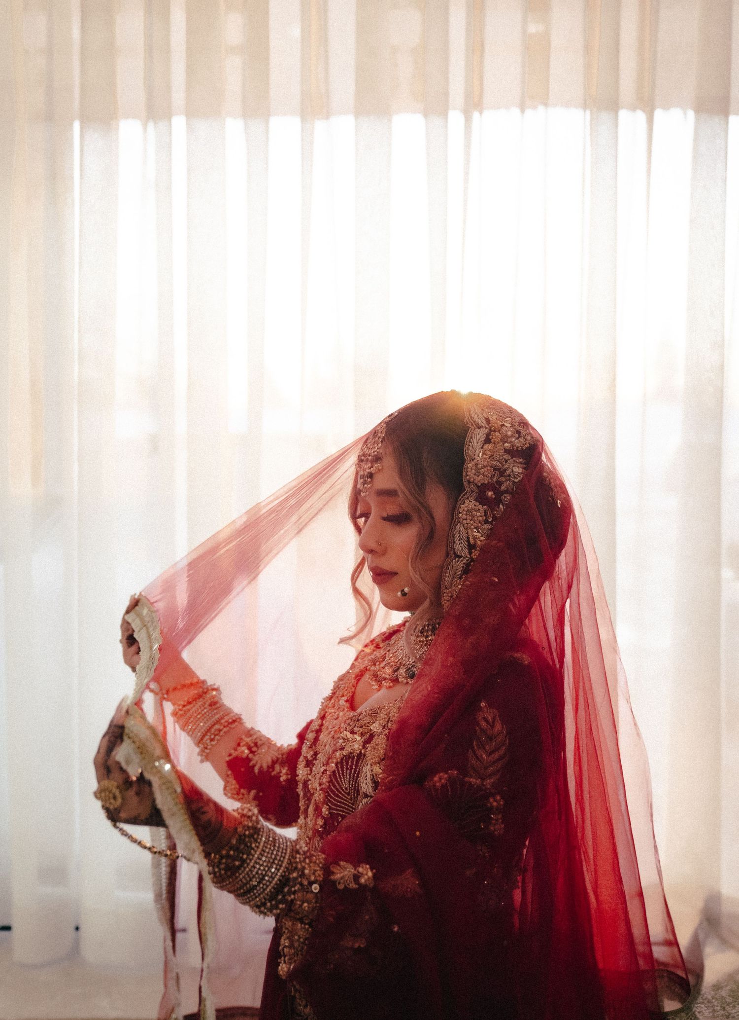 Elegant figure in a red veil poses gracefully against white curtains.