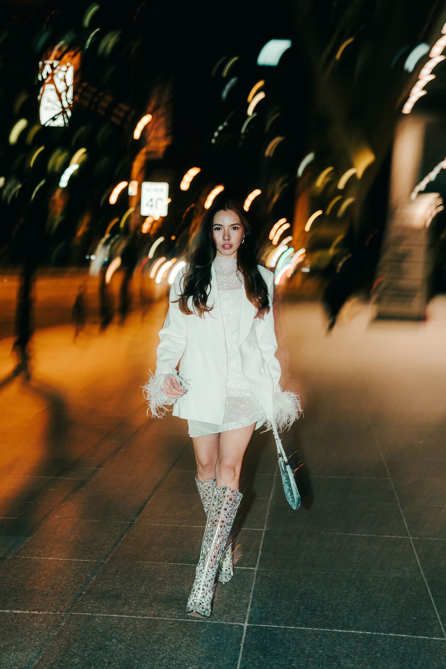 Person in a white dress and sparkly boots walking on a dark street at night.
