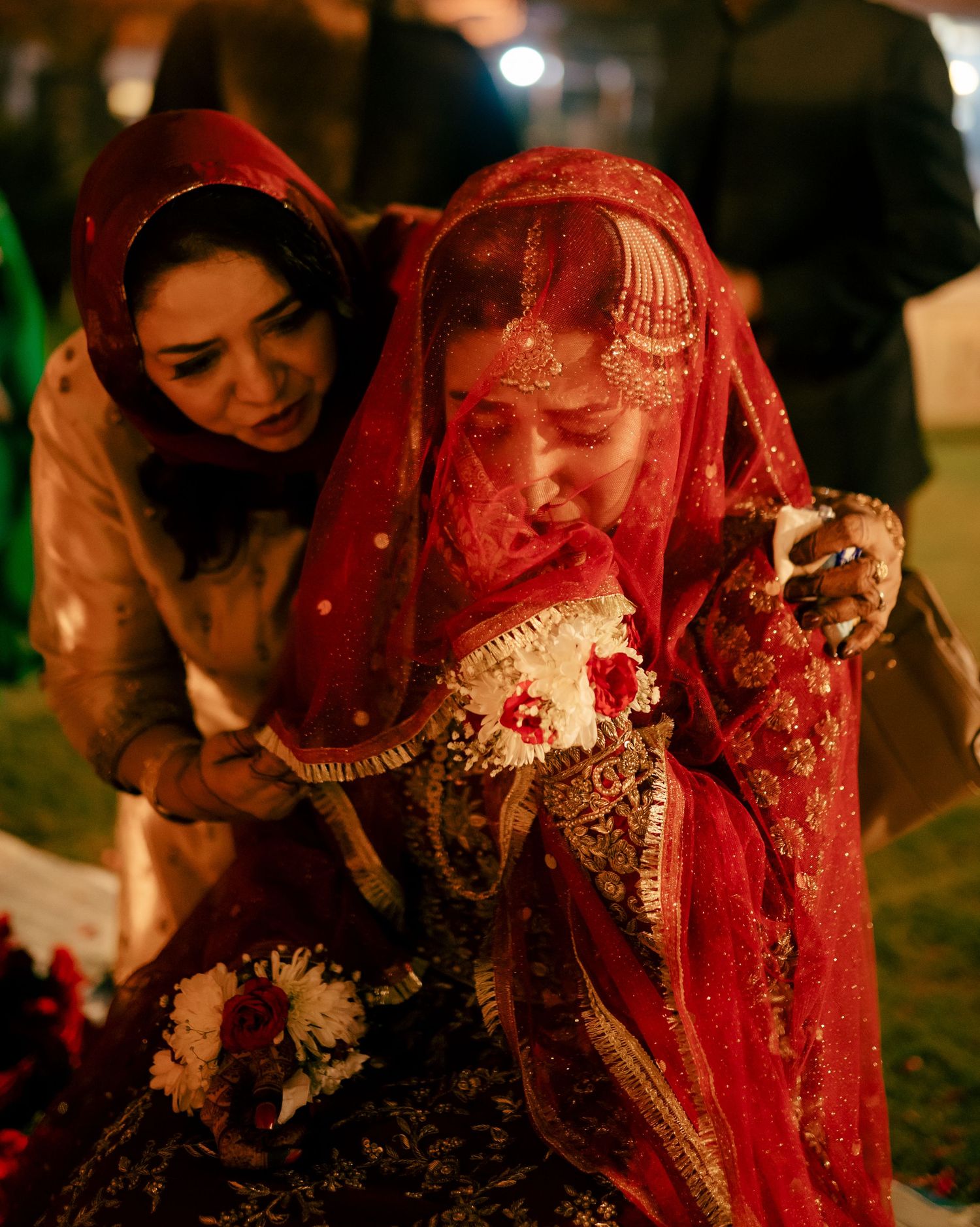 Traditional wedding ceremony with bride in red veil and ornate dress during evening celebration.