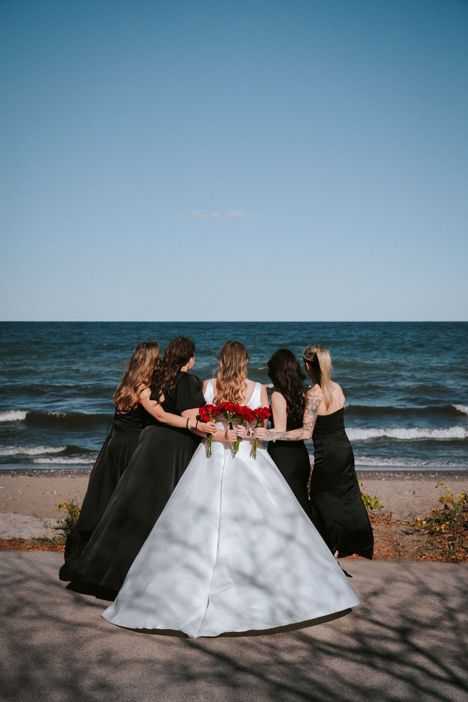 Three people in formal attire sit together on a beach with waves in the background.