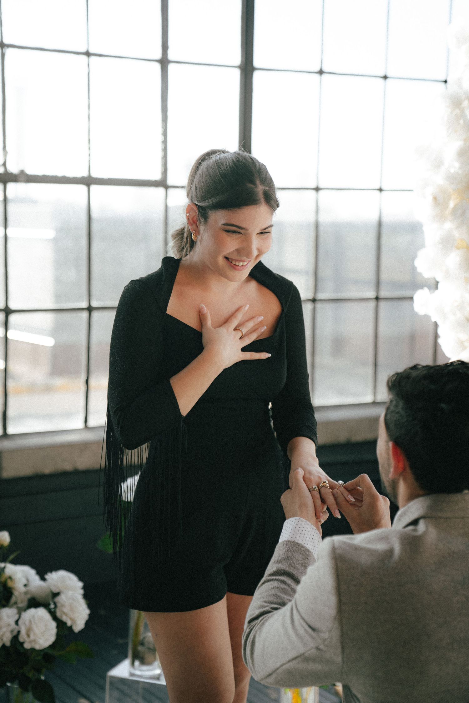 An emotional proposal moment unfolds in a modern industrial space with white balloon decorations.