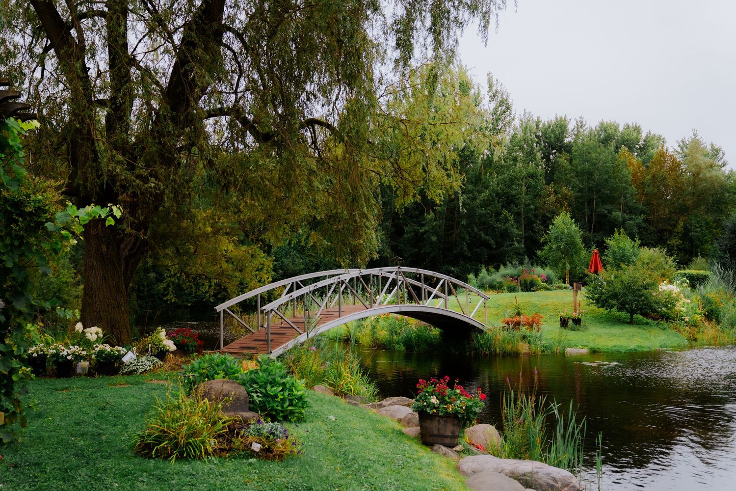 Scenic garden landscape with a pond, willow trees, and winding pathway through lush greenery.