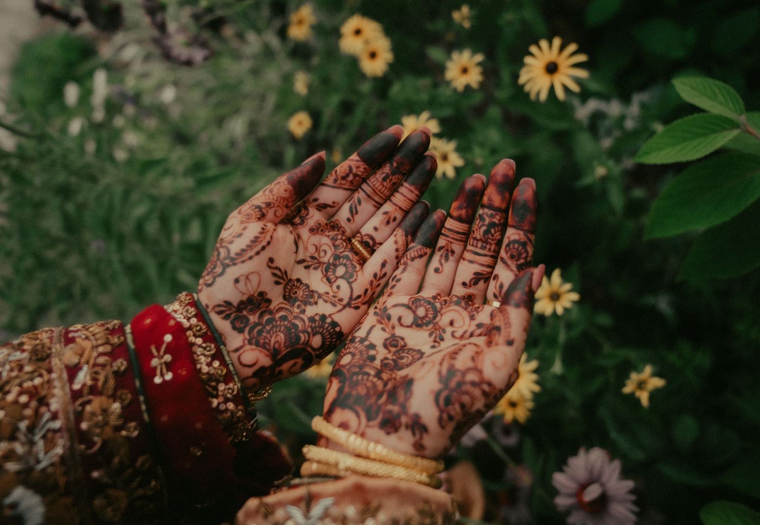 Intricate henna designs adorn hands with yellow flowers in garden background.