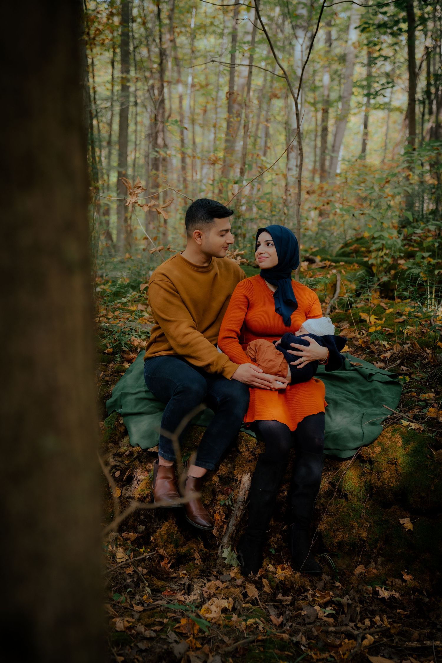 Cozy forest engagement photos with couple in orange and black outfits sitting on fallen logs.