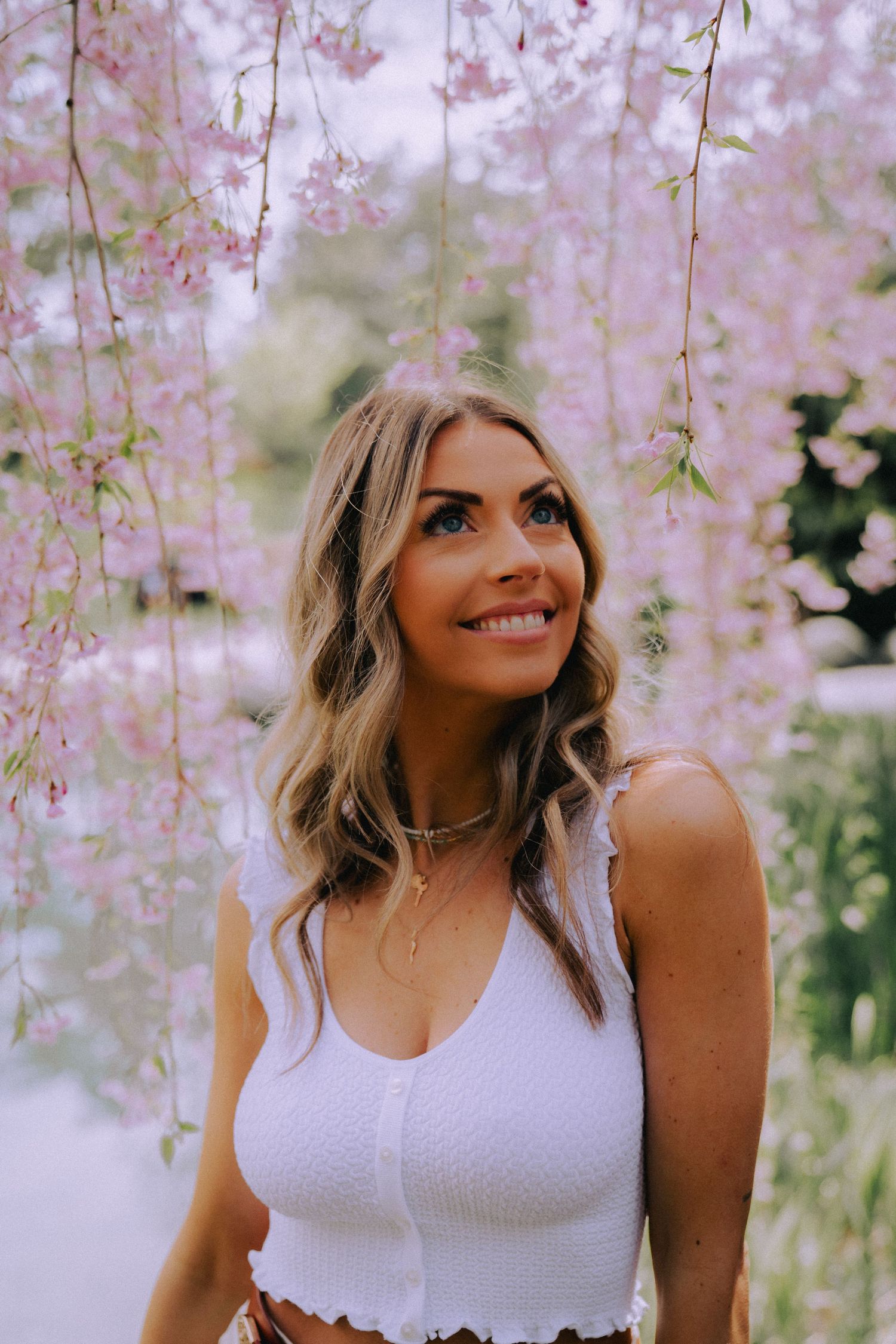 Spring fashion portrait under delicate pink cherry blossoms with white tank top.