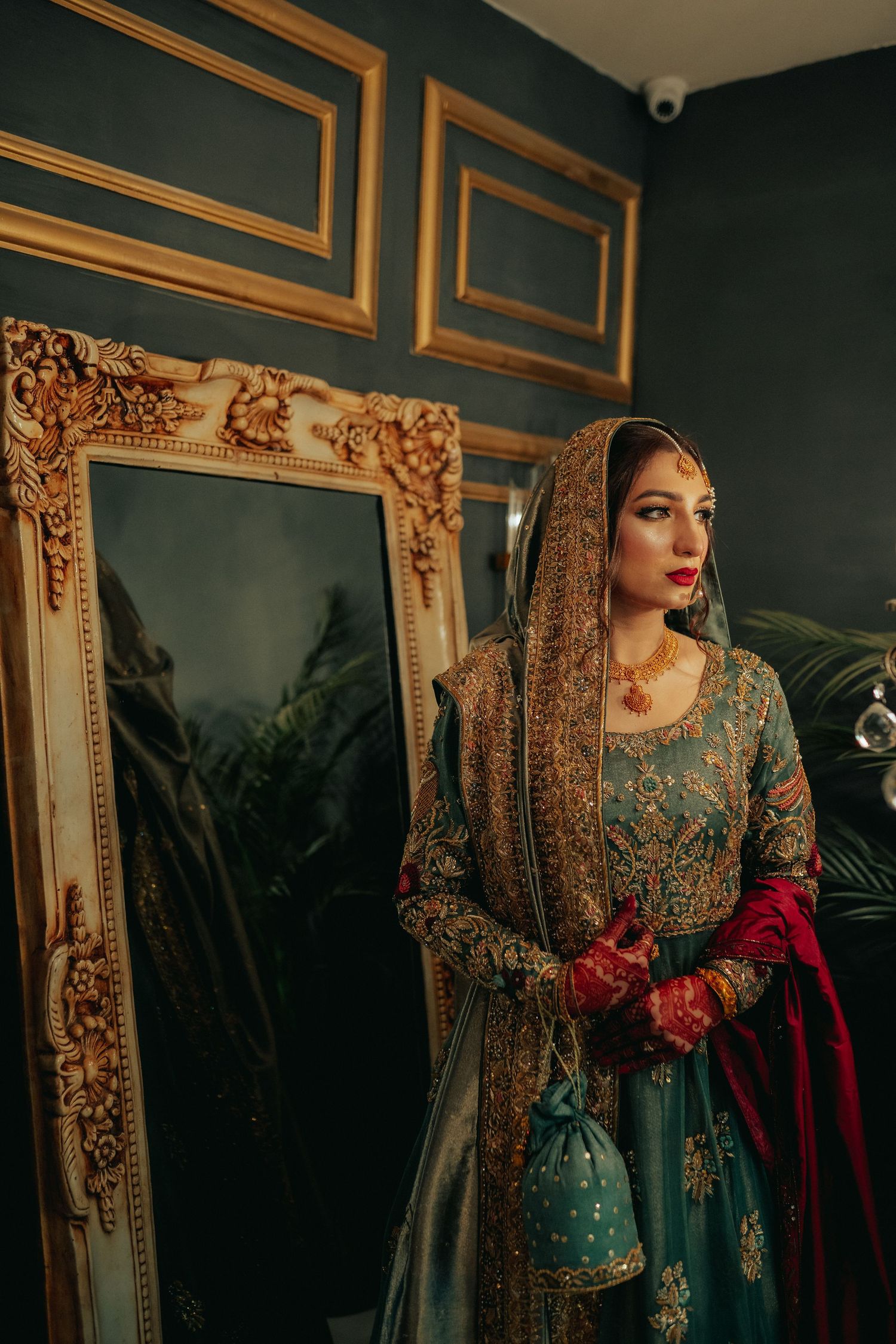 Elegant bridal portrait with ornate gold-framed mirrors and dramatic lighting.