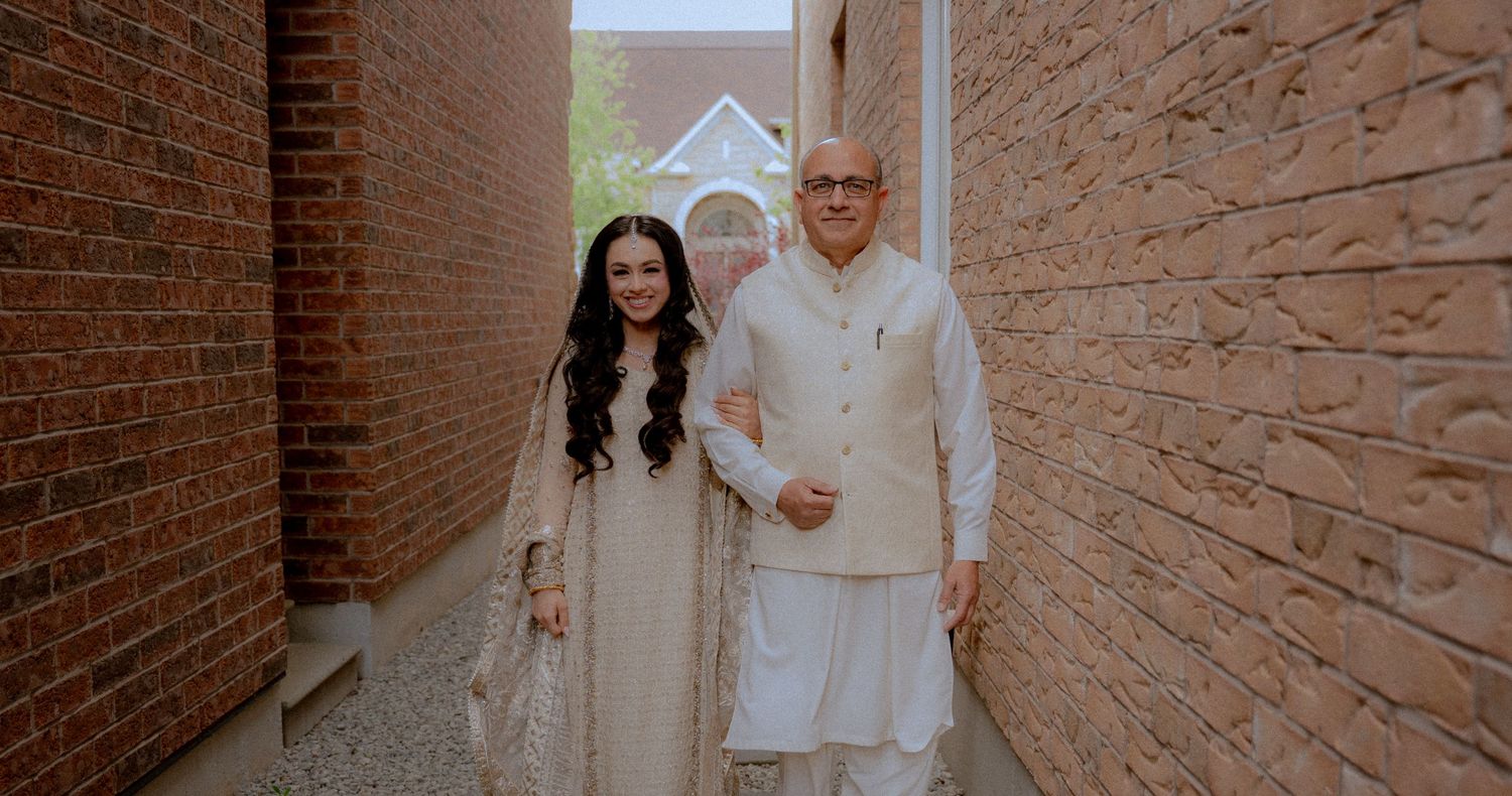 Wedding group poses along rustic brick wall in coordinated white attire.