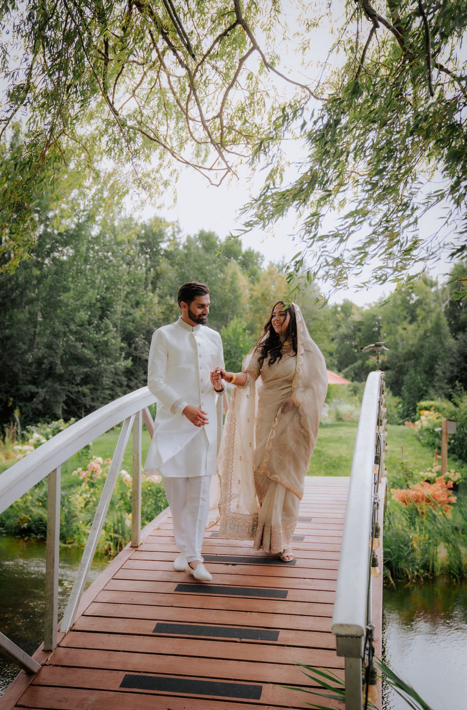 Couple walking on a wooden dock over a serene pond surrounded by lush greenery.