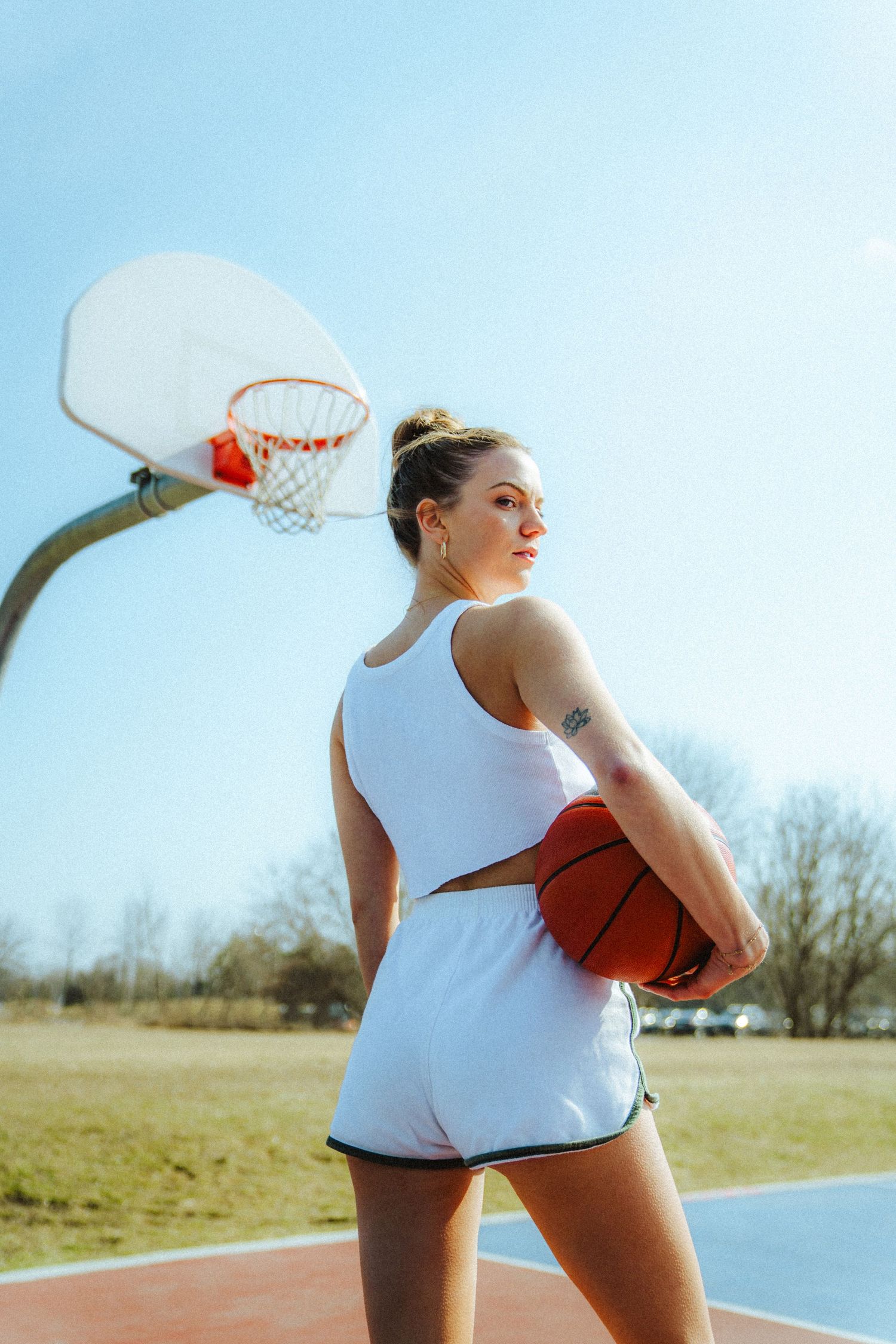 Athletic scene on outdoor basketball court with white tank top and basketball.