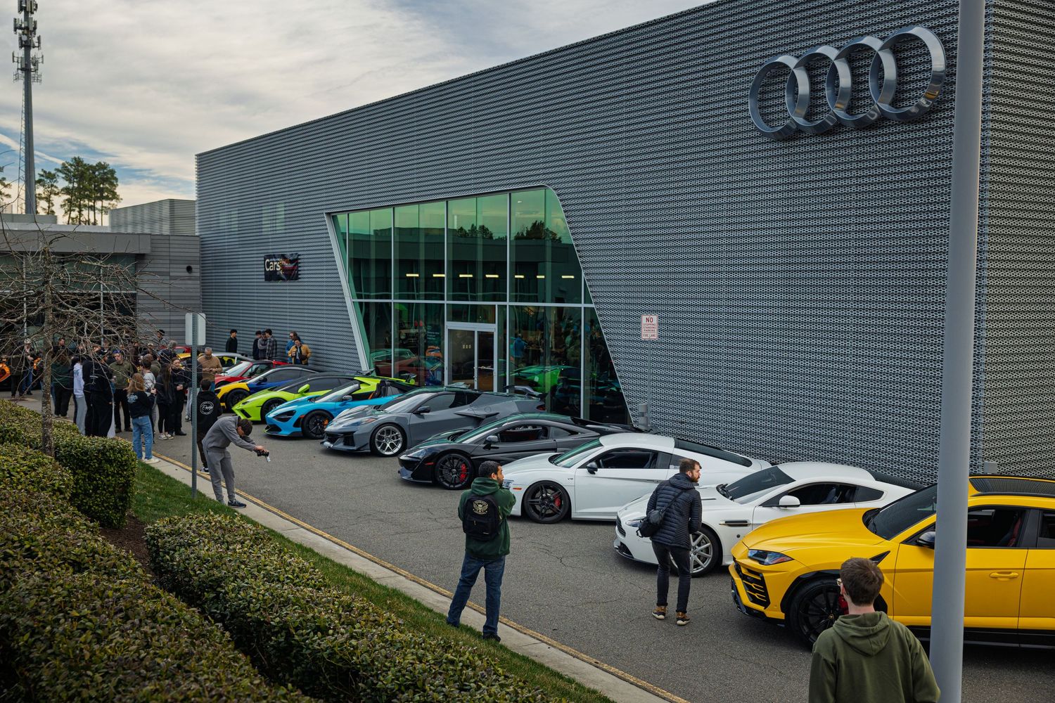 Modern Audi dealership exterior with multiple vehicles on display in the showroom and parking lot.