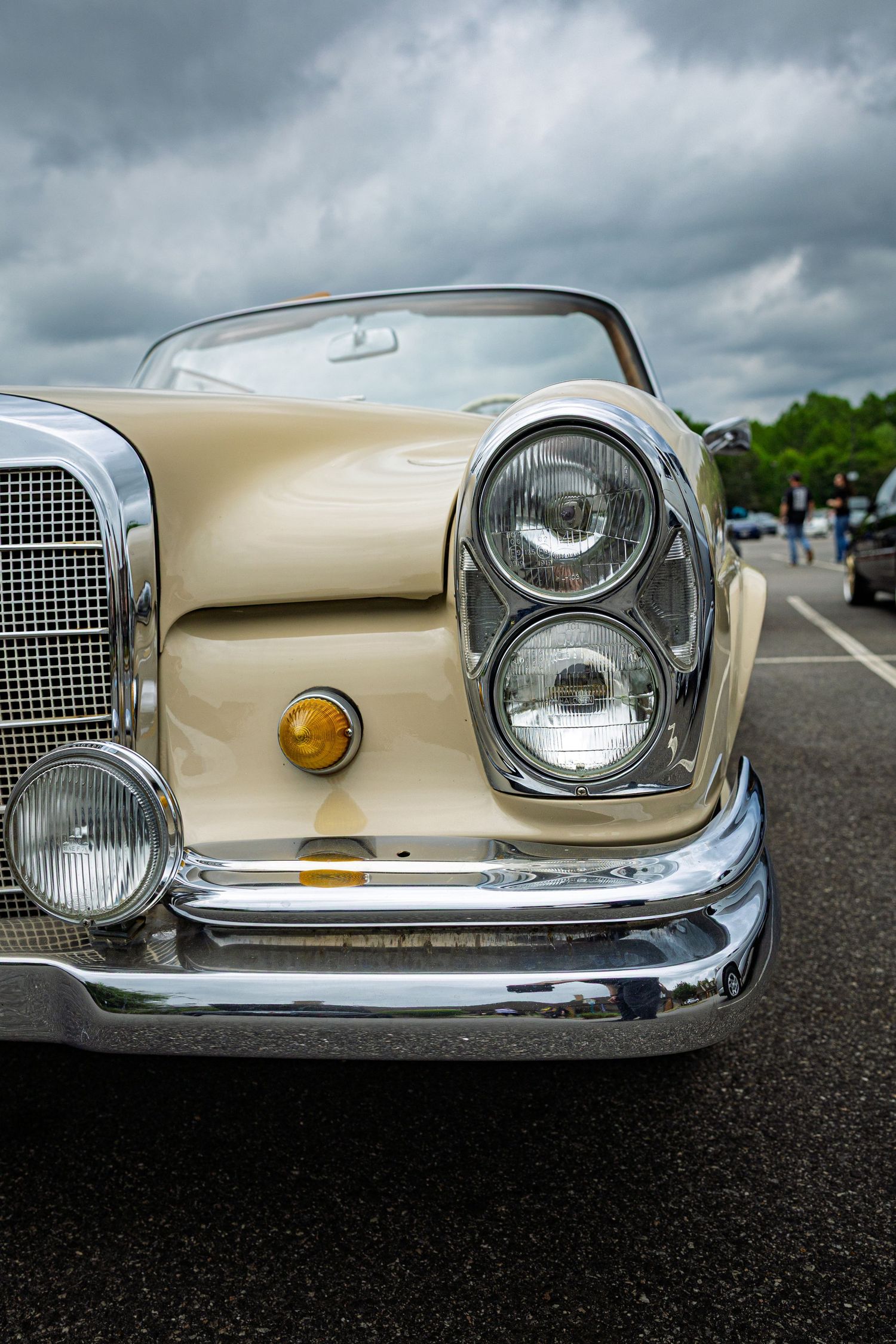 Close-up view of vintage Mercedes-Benz front end showing classic chrome headlights and grille against stormy sky.