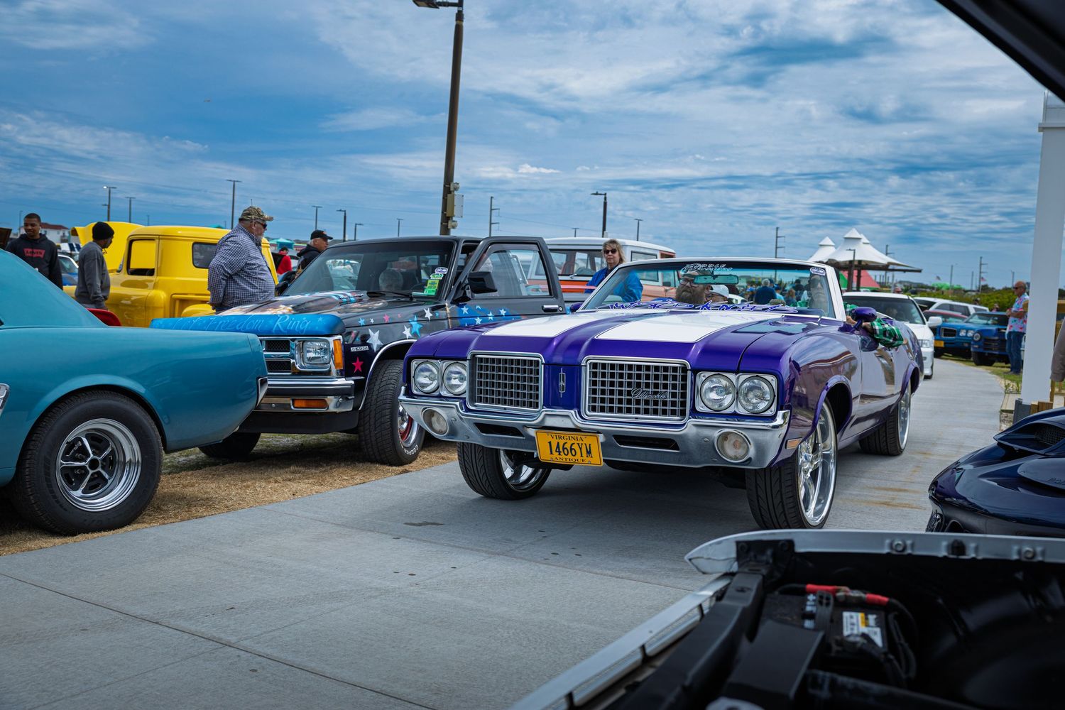 Vintage purple classic car at an outdoor car show with colorful vehicles on a cloudy day.