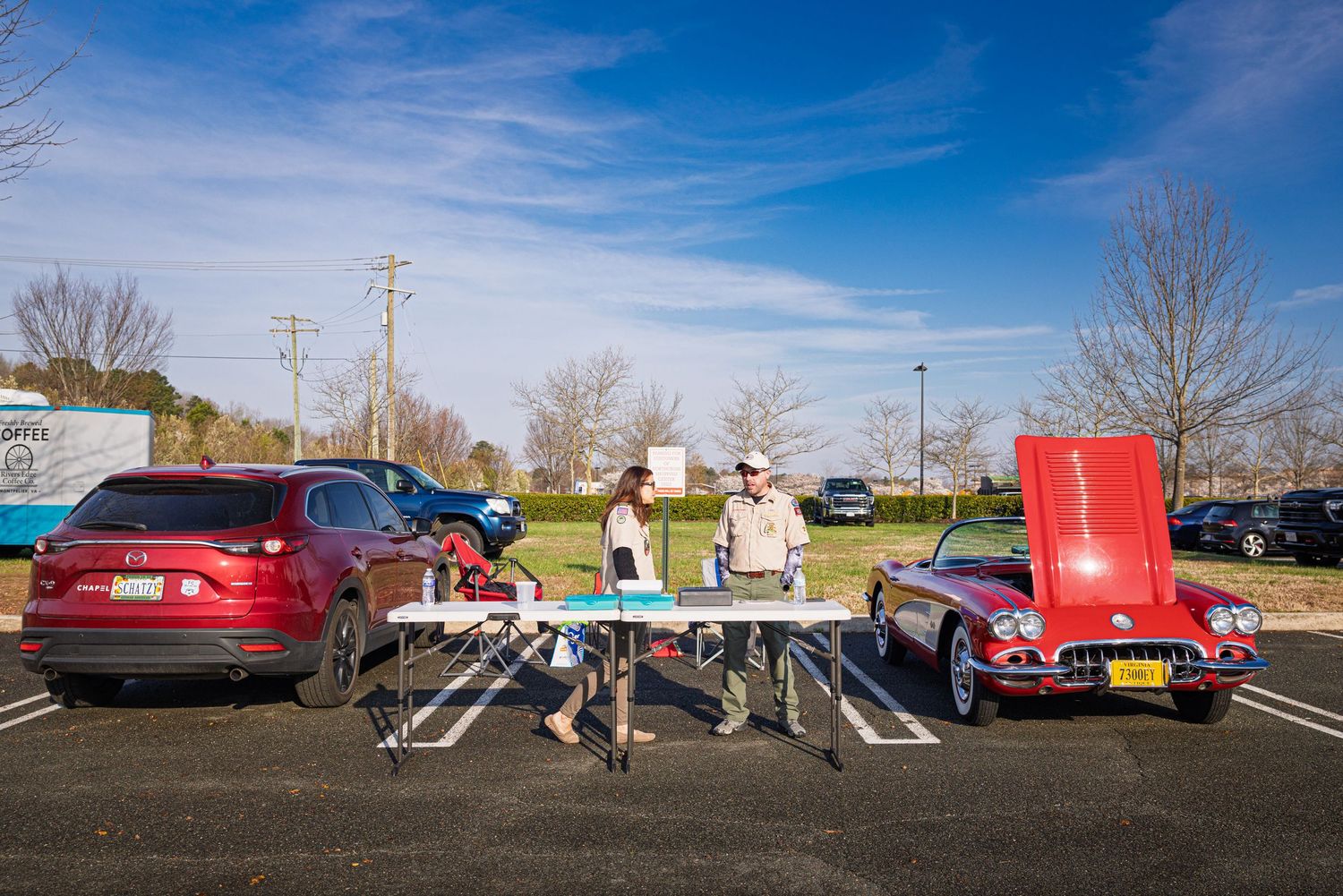 A panoramic view of a parking lot with several cars and people gathering during a daytime event.