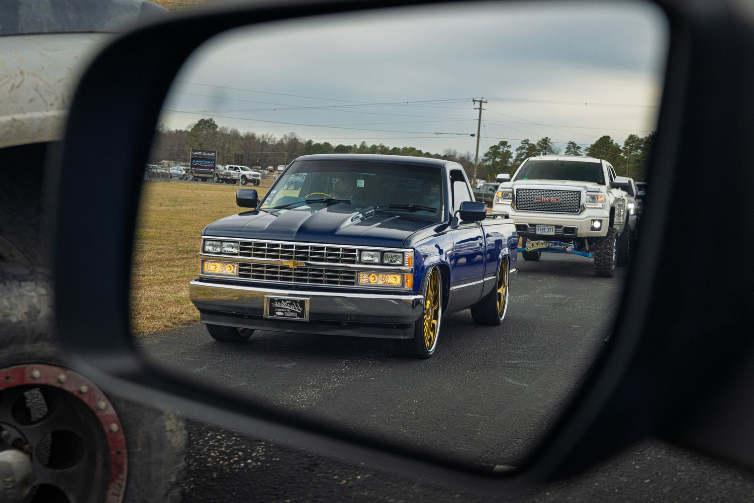 Classic vintage cars lined up in a parking lot viewed through a car side mirror reflection.