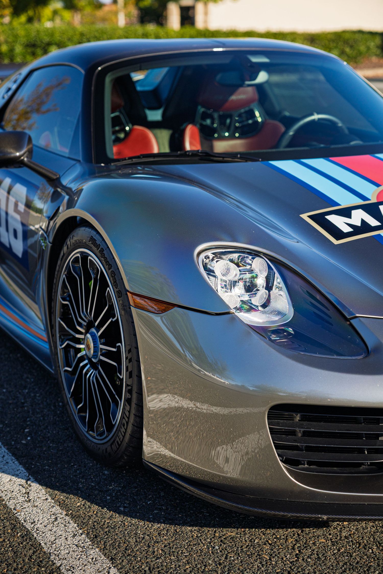 Close-up view of a sleek gray Porsche 918 Spyder with racing stripes and black alloy wheels parked on asphalt.