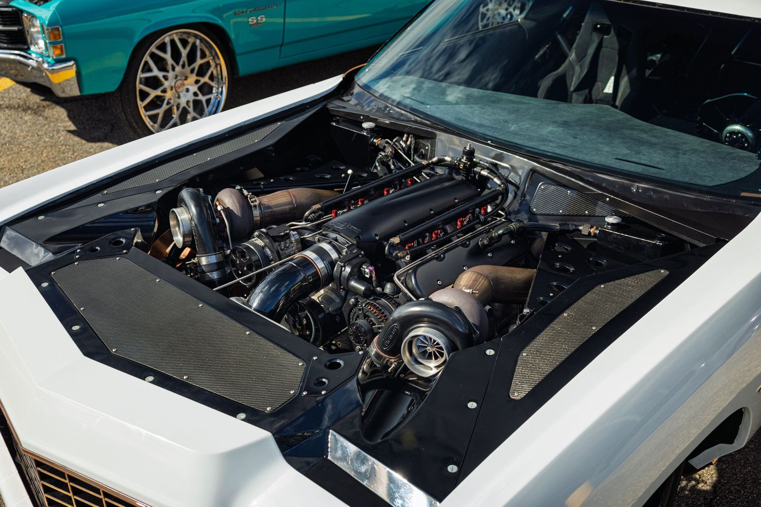 Custom engine bay of a white Chevrolet showing a modified turbocharged engine setup with chrome components.