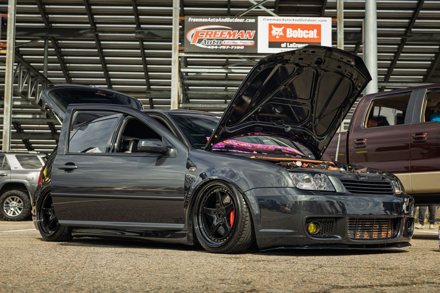 A lowered black car with red accented wheels parked in a covered area.