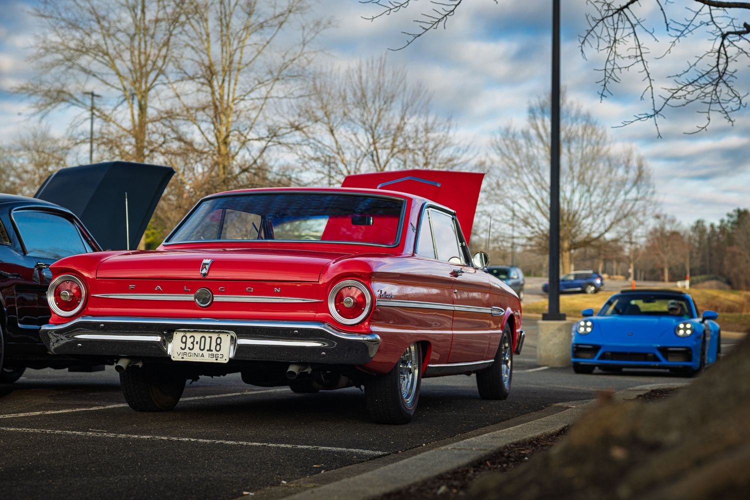 A classic red Ford Galaxie parked next to a modern blue sports car at a car show on a sunny day.