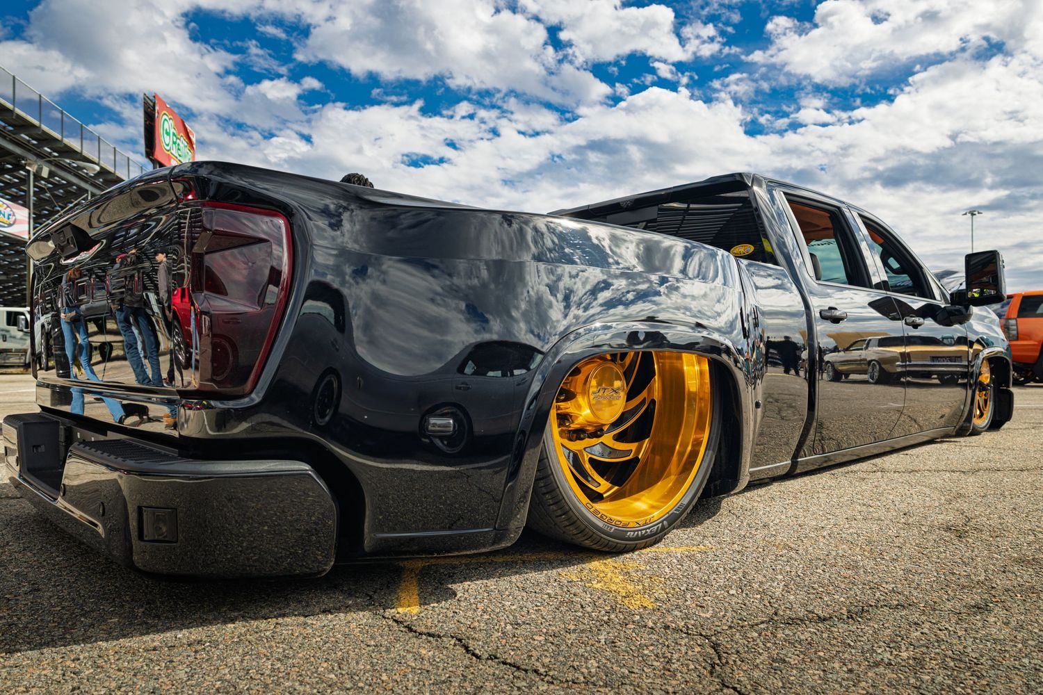 Low-angle view of modified trucks with custom wheels and suspension setups against a blue sky.