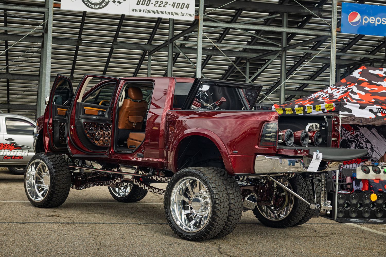 Custom trucks with lifted suspensions and oversized wheels displayed at an outdoor automotive show.