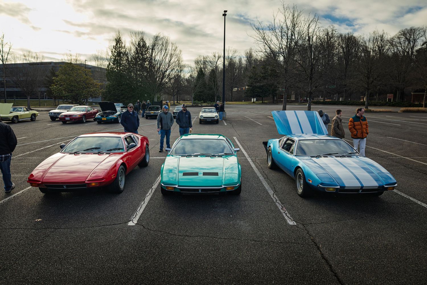Classic sports cars including Corvettes and other vintage automobiles lined up in a parking lot under cloudy skies.