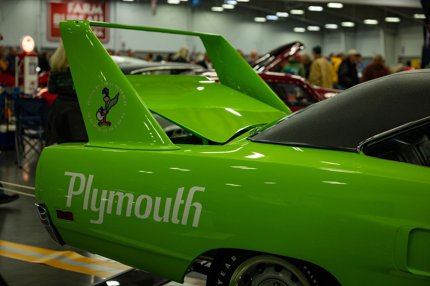 Bright green Plymouth Superbird classic muscle car with distinctive rear wing on display at indoor auto show.
