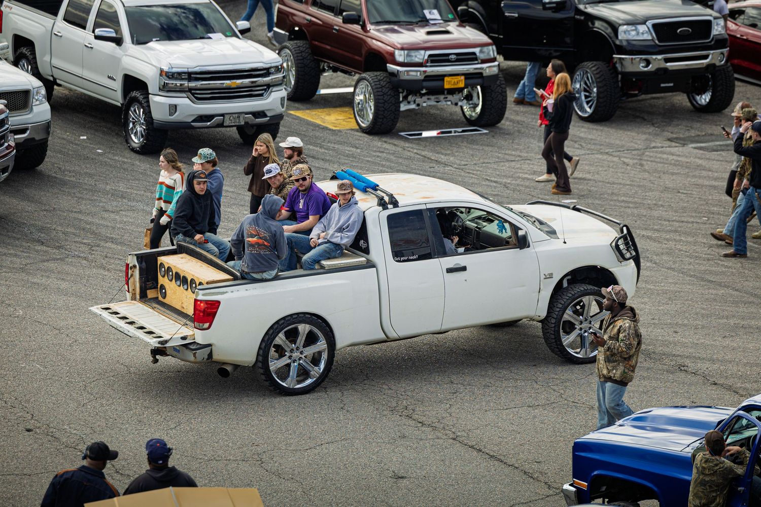Car enthusiasts gather around custom vehicles at an outdoor car show displaying modified trucks and cars.