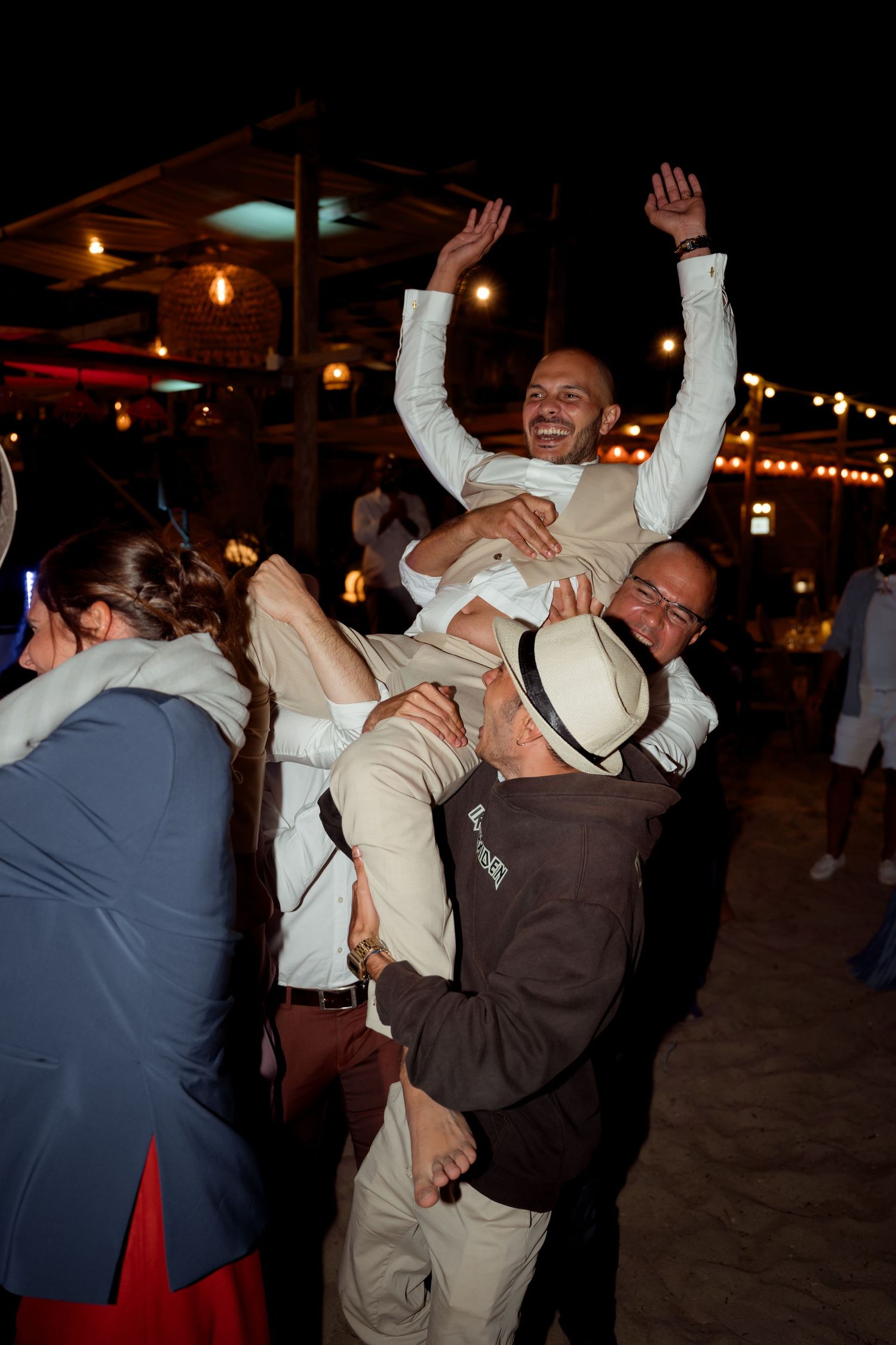 Joyful groom lifted by wedding guests with arms raised in celebration.