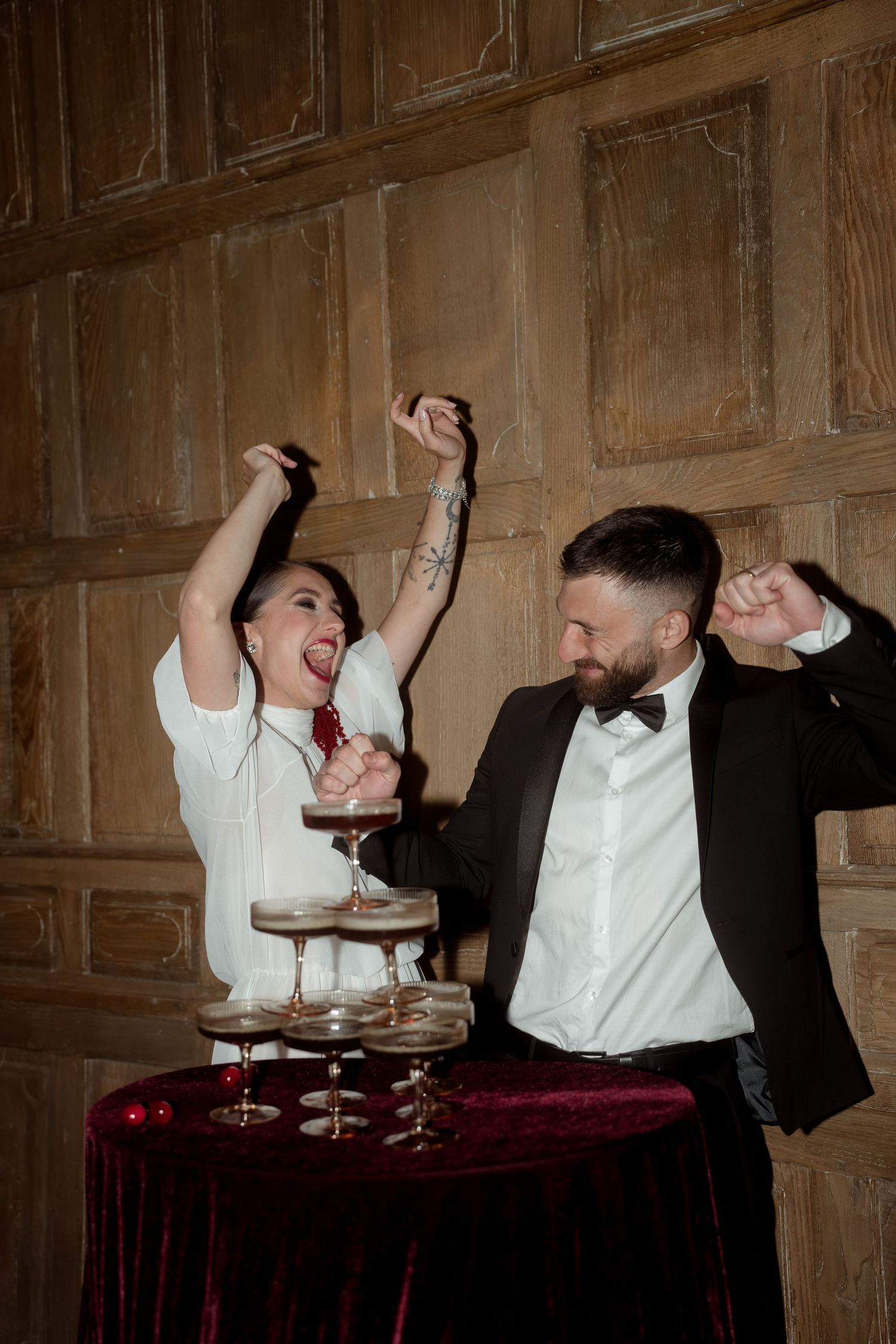 Joyful bride and groom celebrate with champagne tower, dancing and laughing at wedding reception.