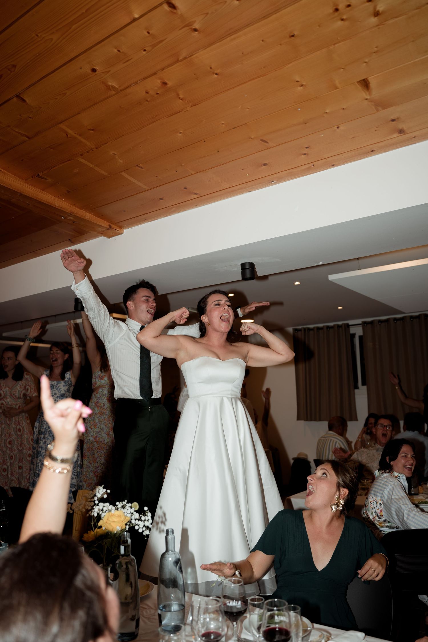 Joyful bride in white strapless dress celebrates with guests at lively wedding reception.